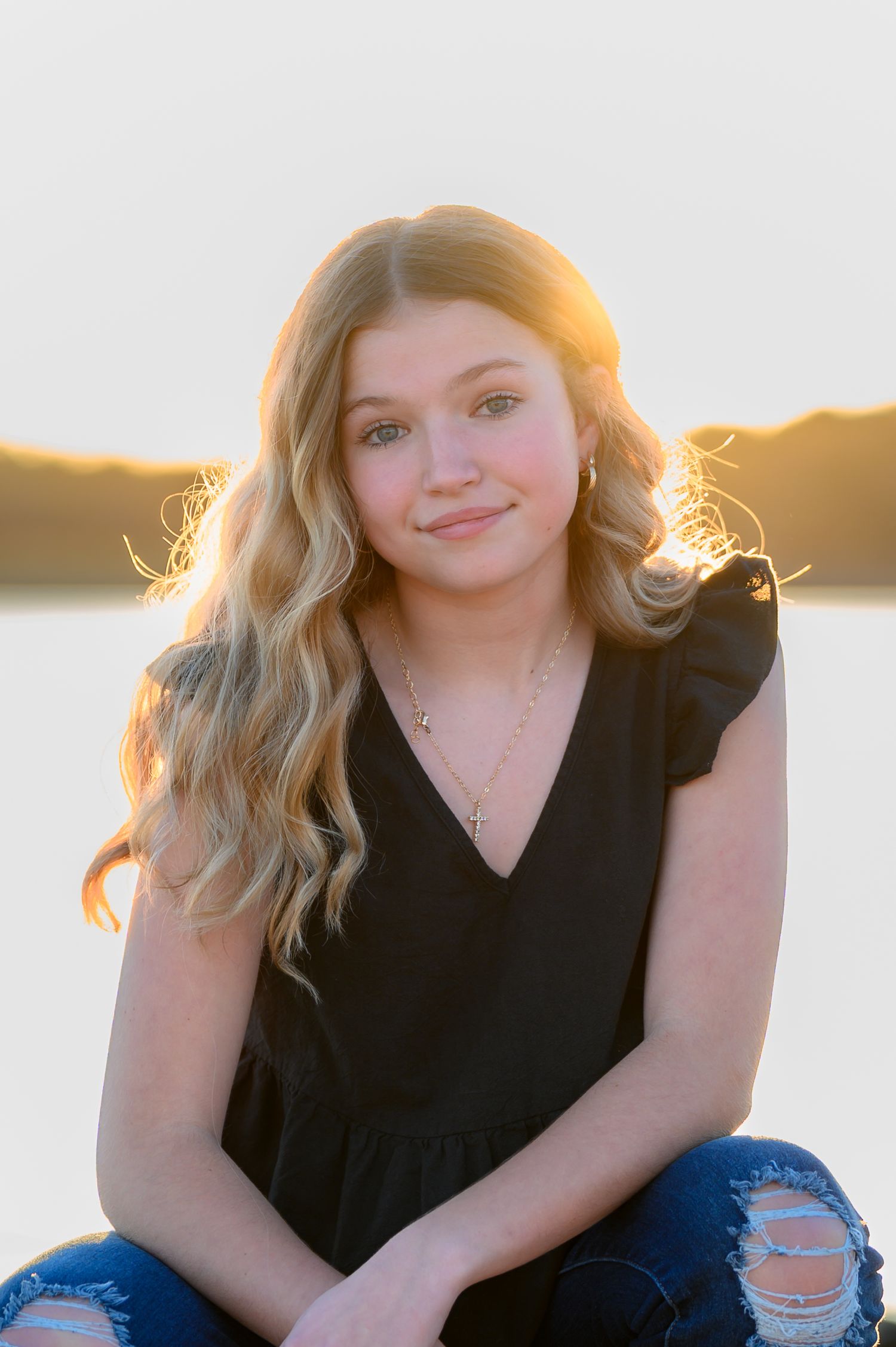 Blonde teenage girl sitting outdoors during a golden sunset portrait session.