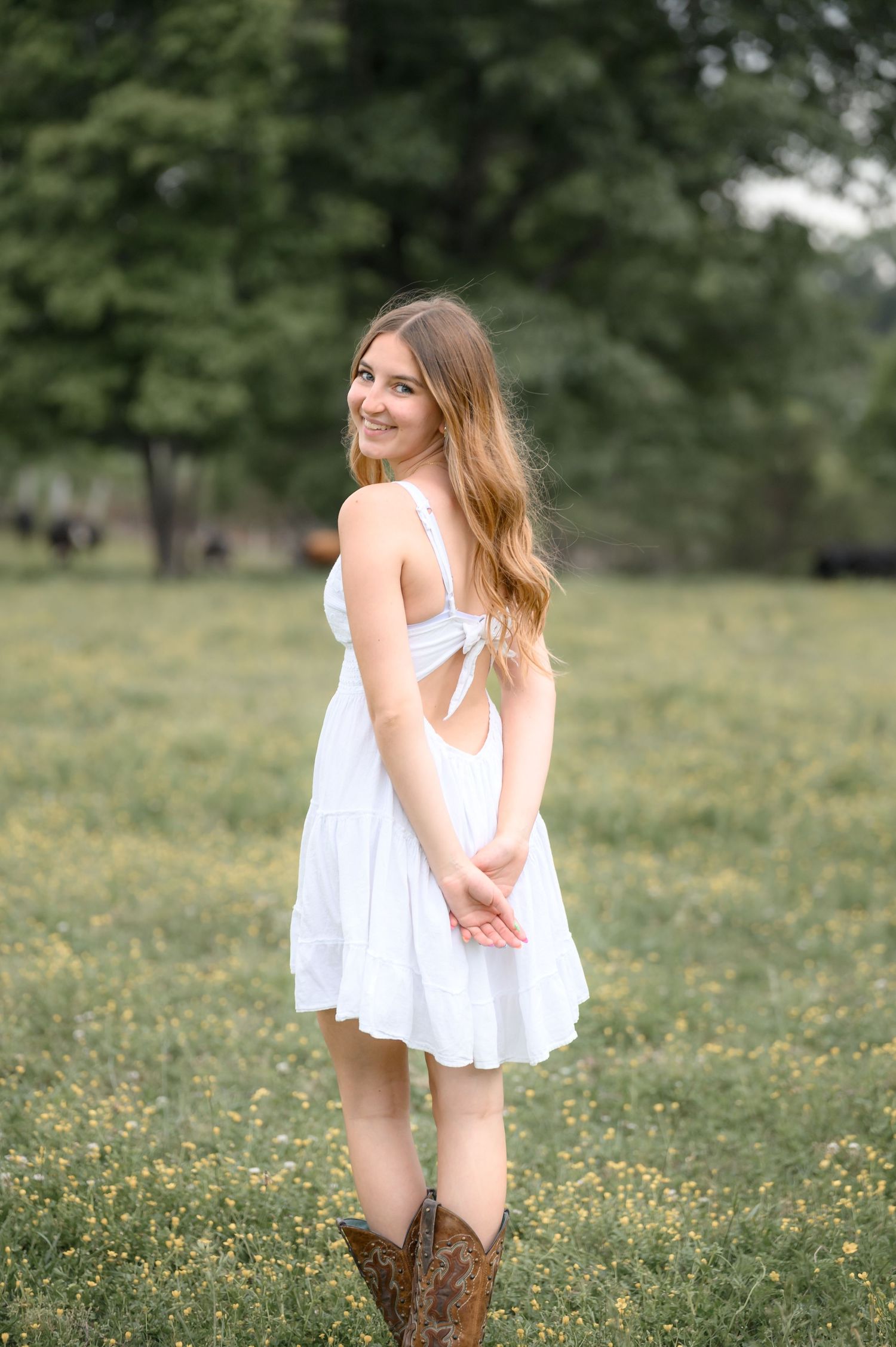 Young woman in white sundress and cowboy boots standing in a wildflower meadow, smiling.
