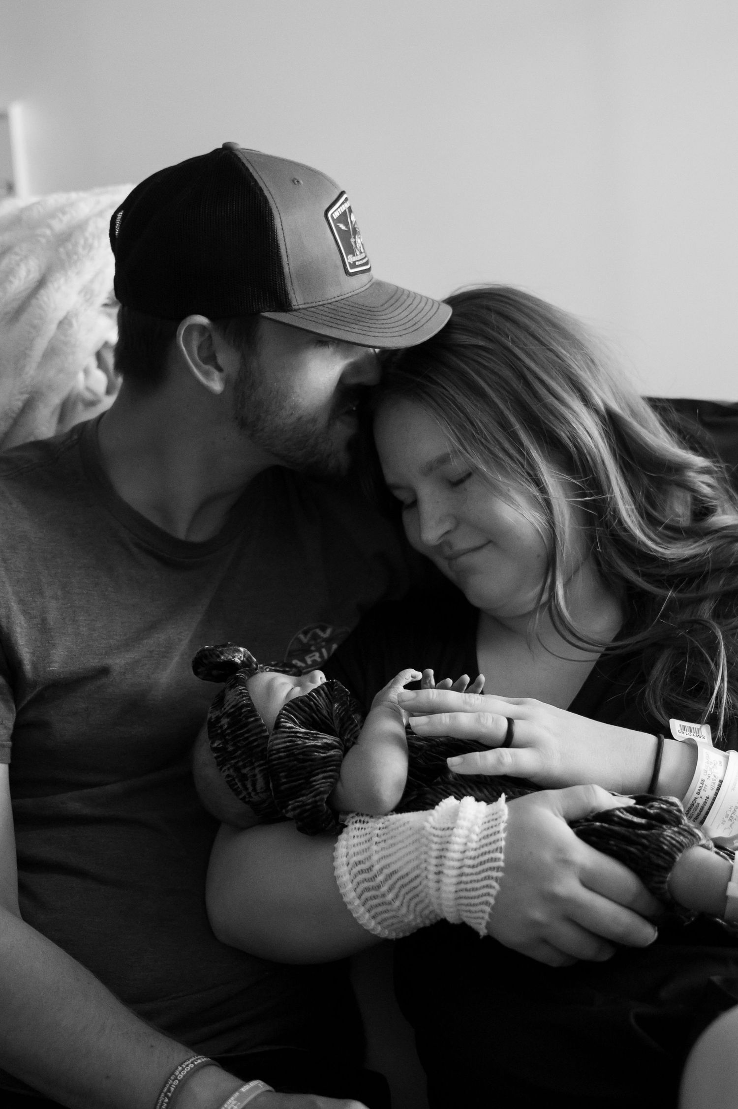 Black and white photo of new parents sitting together and lovingly holding their newborn baby.