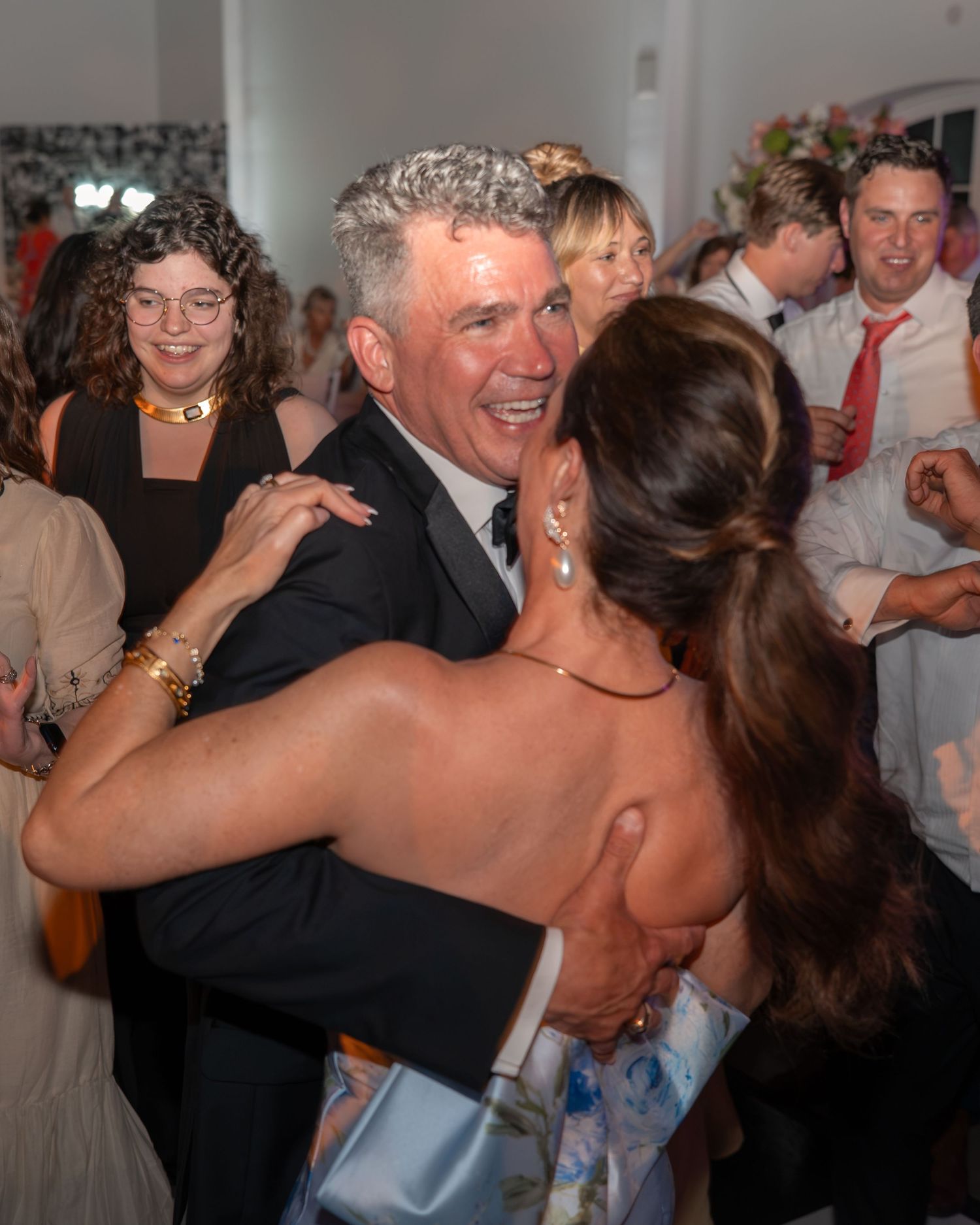 Joyful wedding guest embraces man on crowded dance floor at reception.