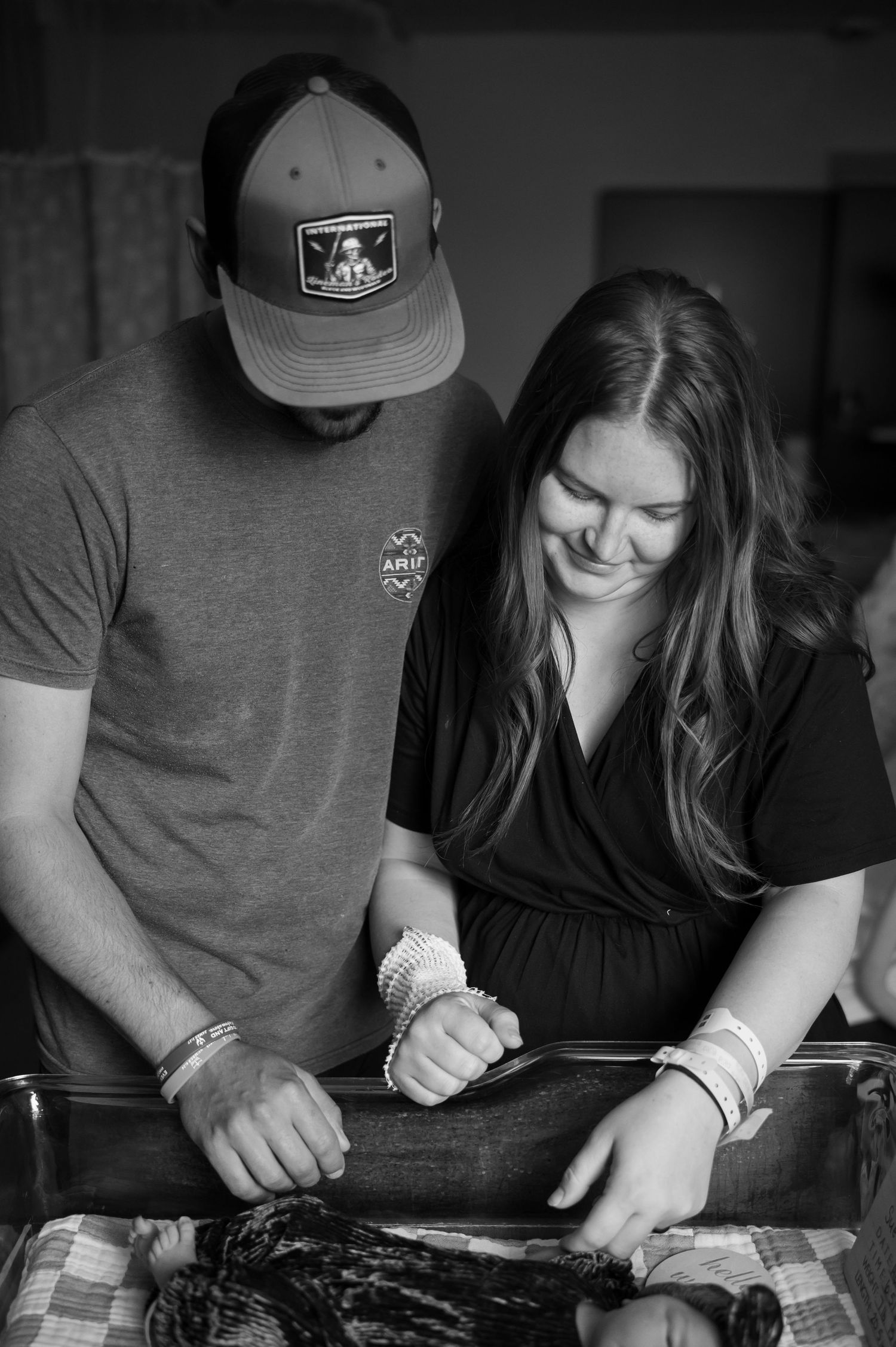 Black and white photo of a couple smiling while tending to their newborn baby together indoors.