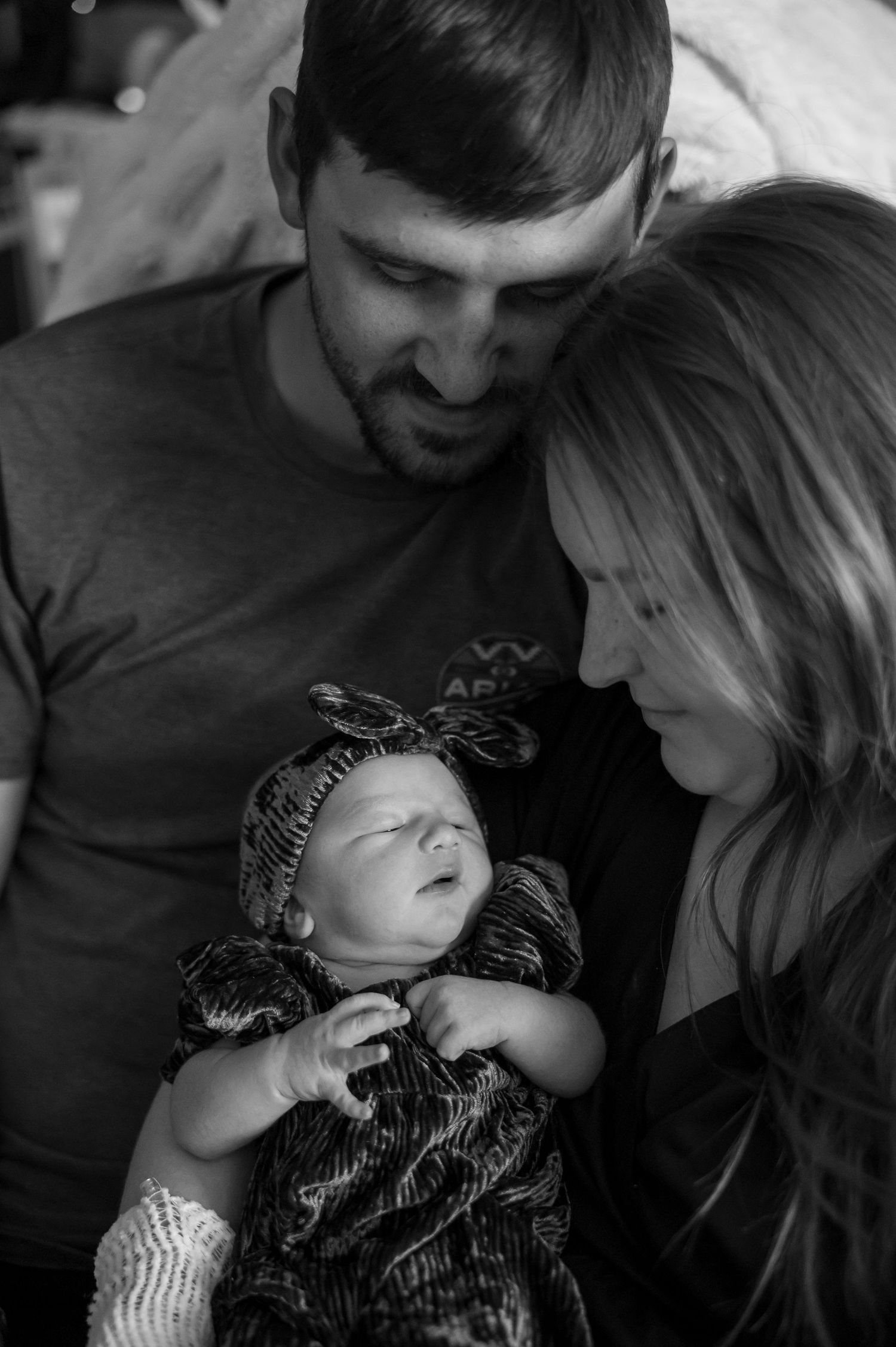 Black and white photo of new parents gazing at their newborn baby dressed in a floral outfit.