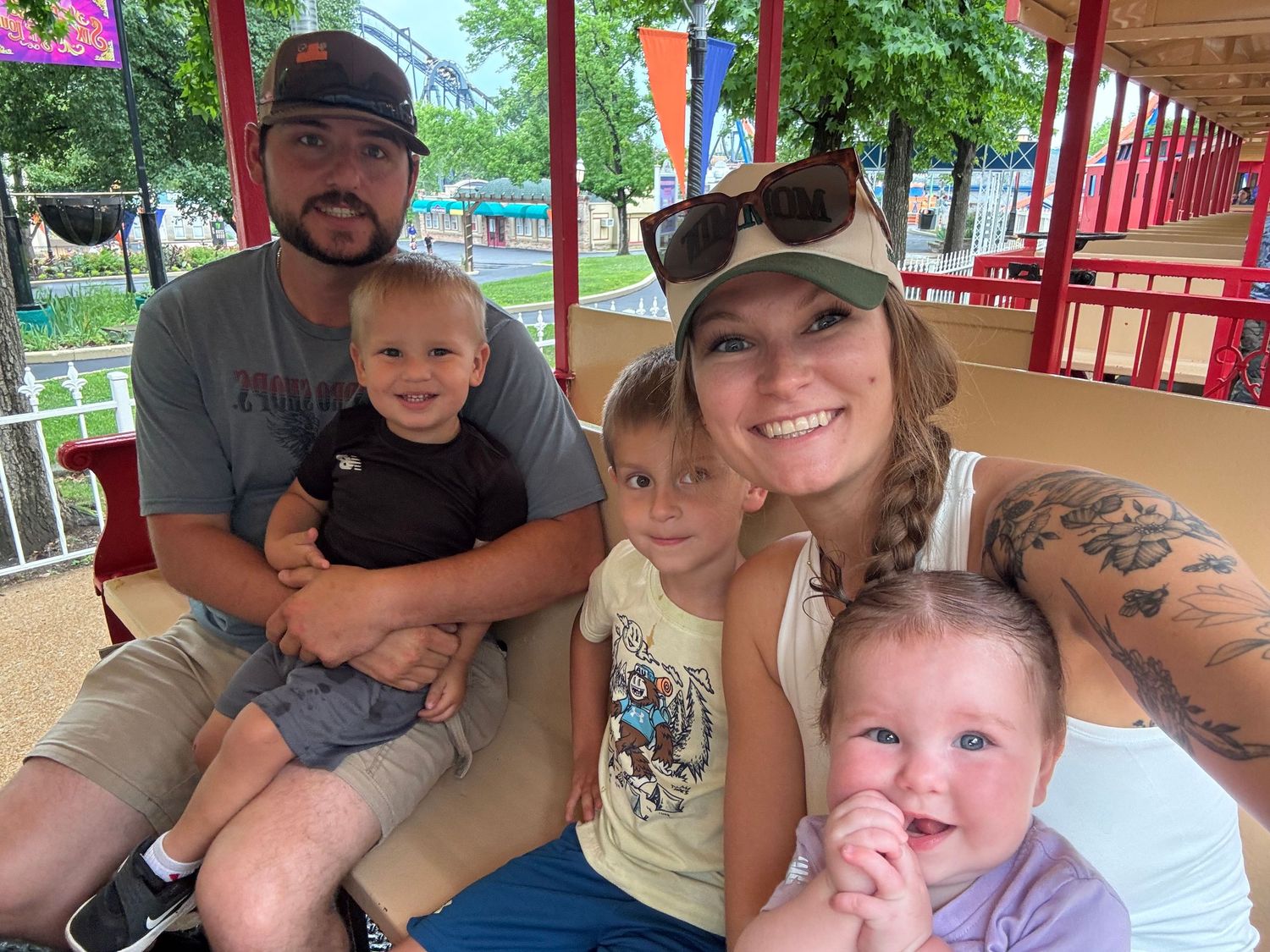 Family of five smiling together at an amusement park, parents with three young children on a ride.
