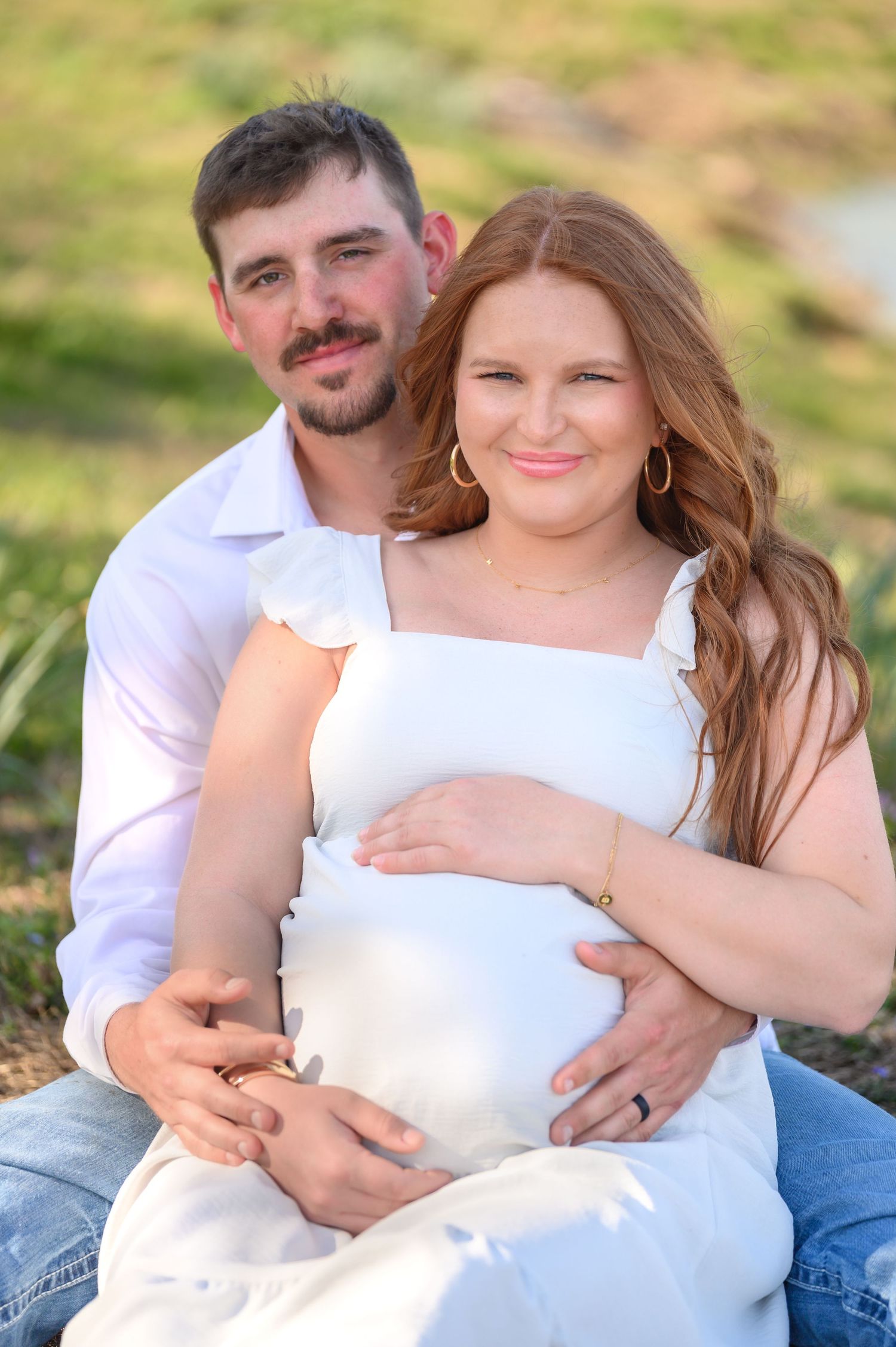 Smiling pregnant couple sitting together outdoors in warm sunlight.