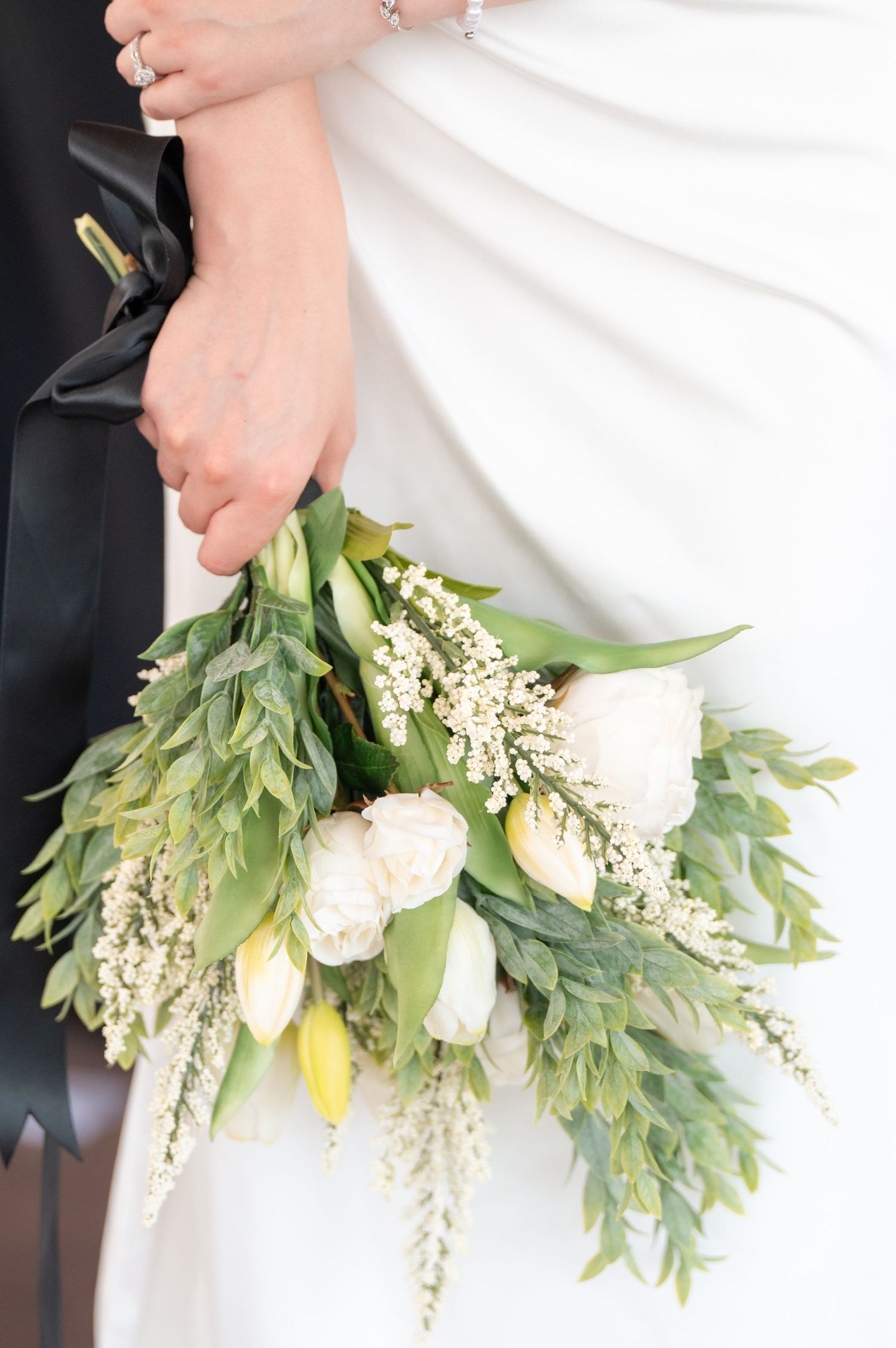 Bride and groom holding a white tulip and greenery wedding bouquet with black ribbon.
