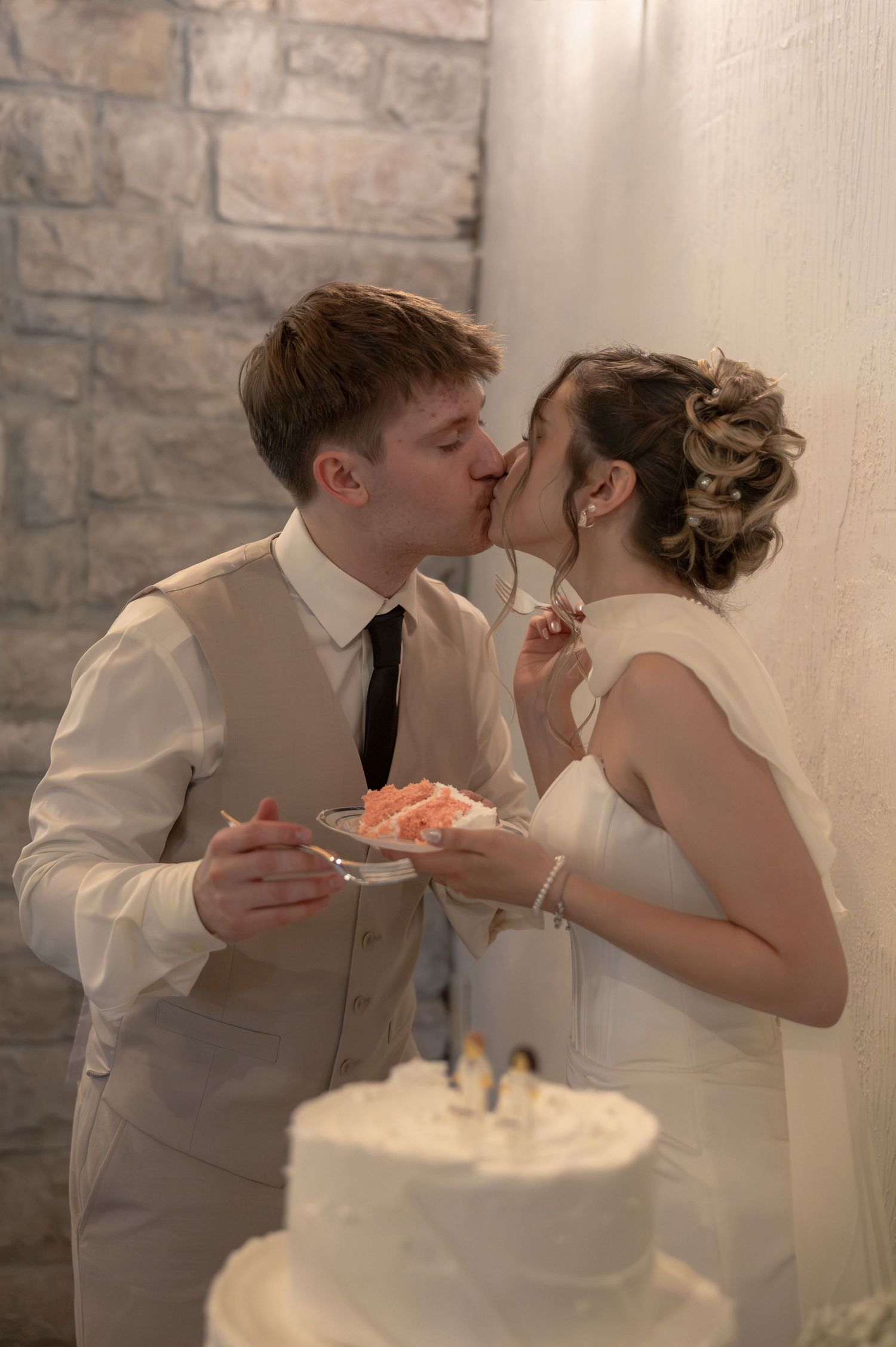Bride and groom sharing a kiss while cutting their white wedding cake with penguin toppers at their reception.