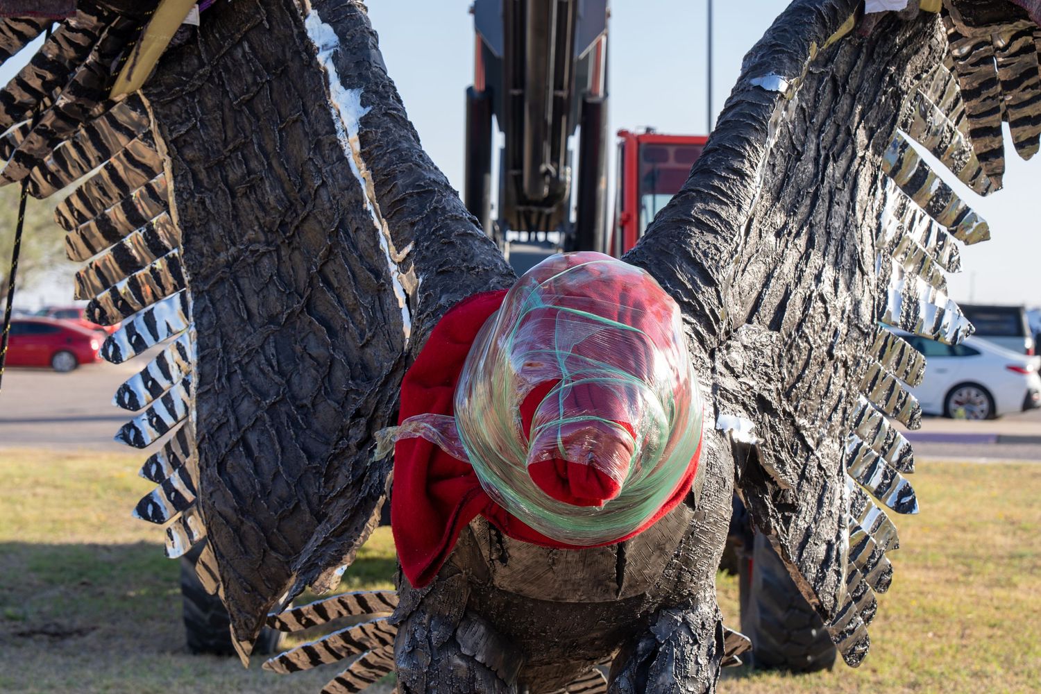 Close-up of a large metal sculpture featuring a helmeted figure with dark textured wings outdoors.