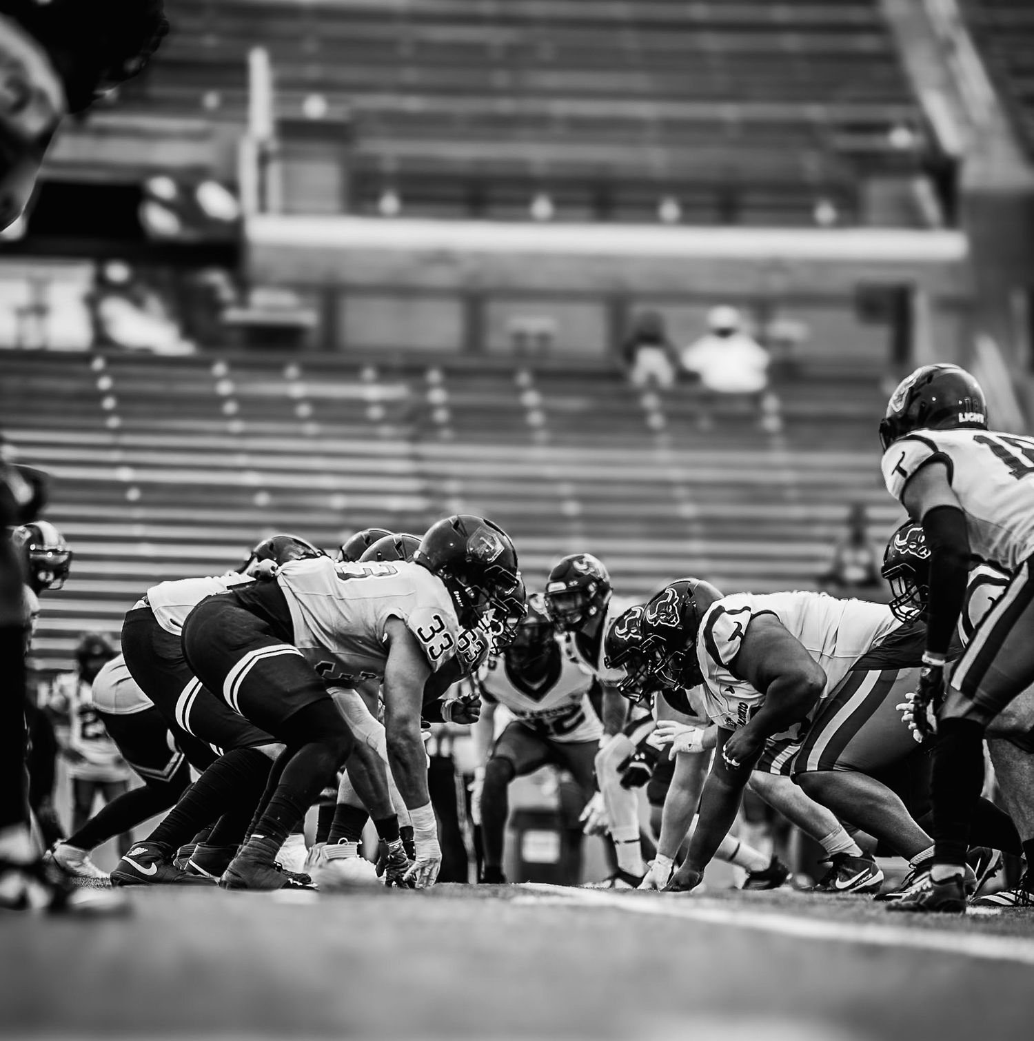 Black and white aerial view of football teams facing off at line of scrimmage in stadium.