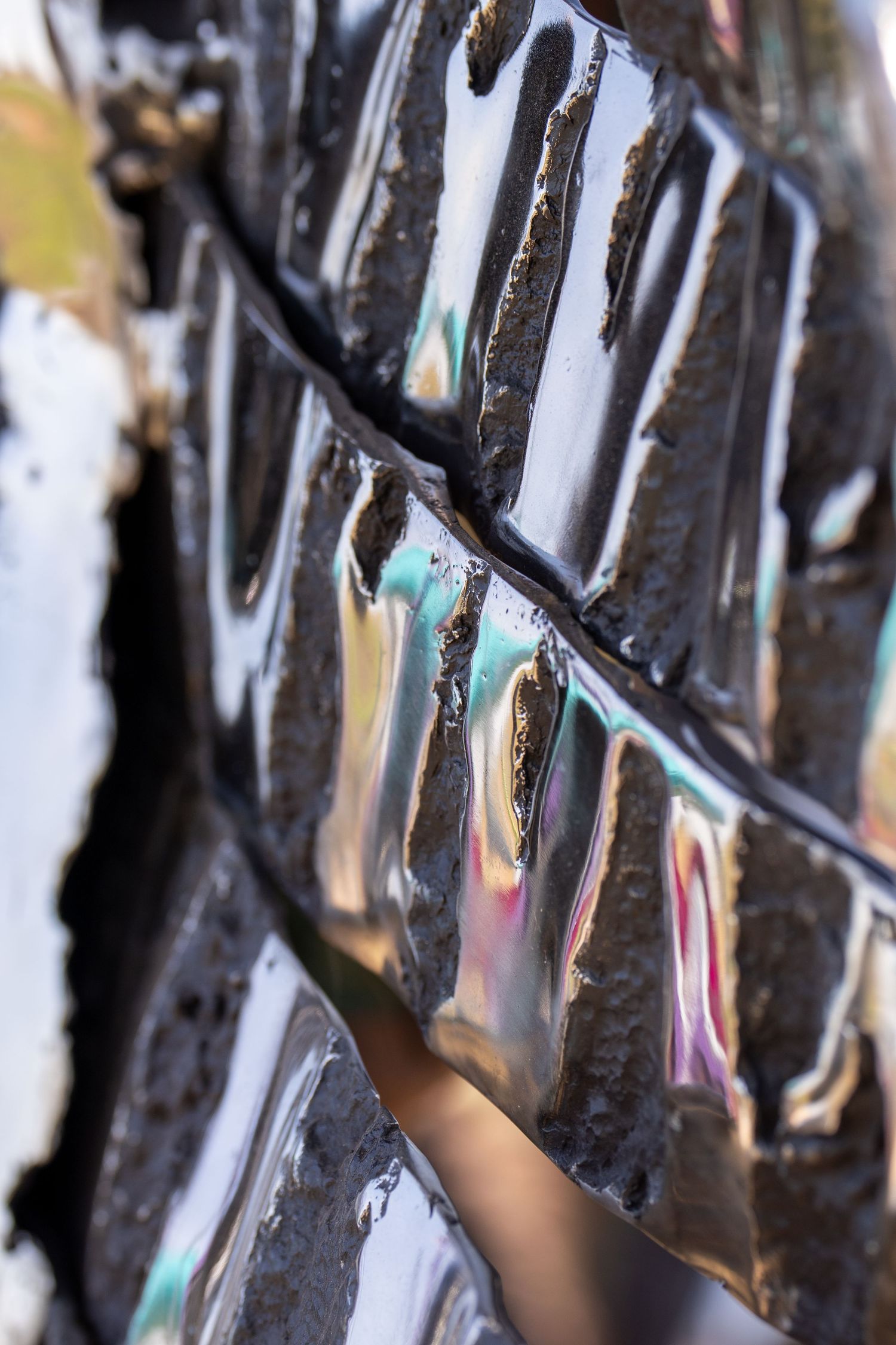 Close-up of glossy black iridescent metal tiles with textured surface on an outdoor sculpture.