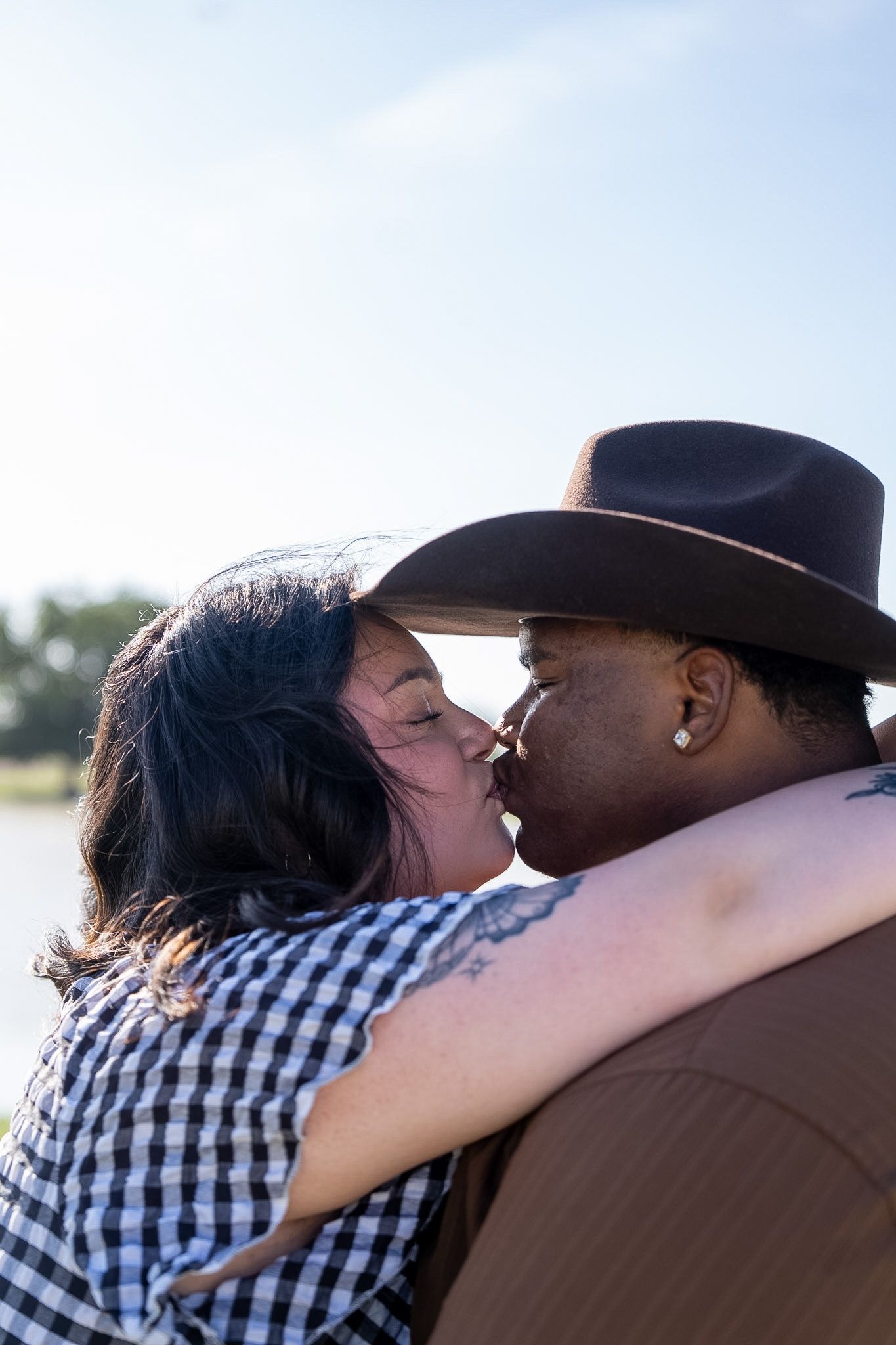 Interracial couple sharing a romantic kiss outdoors, man wearing brown cowboy hat.