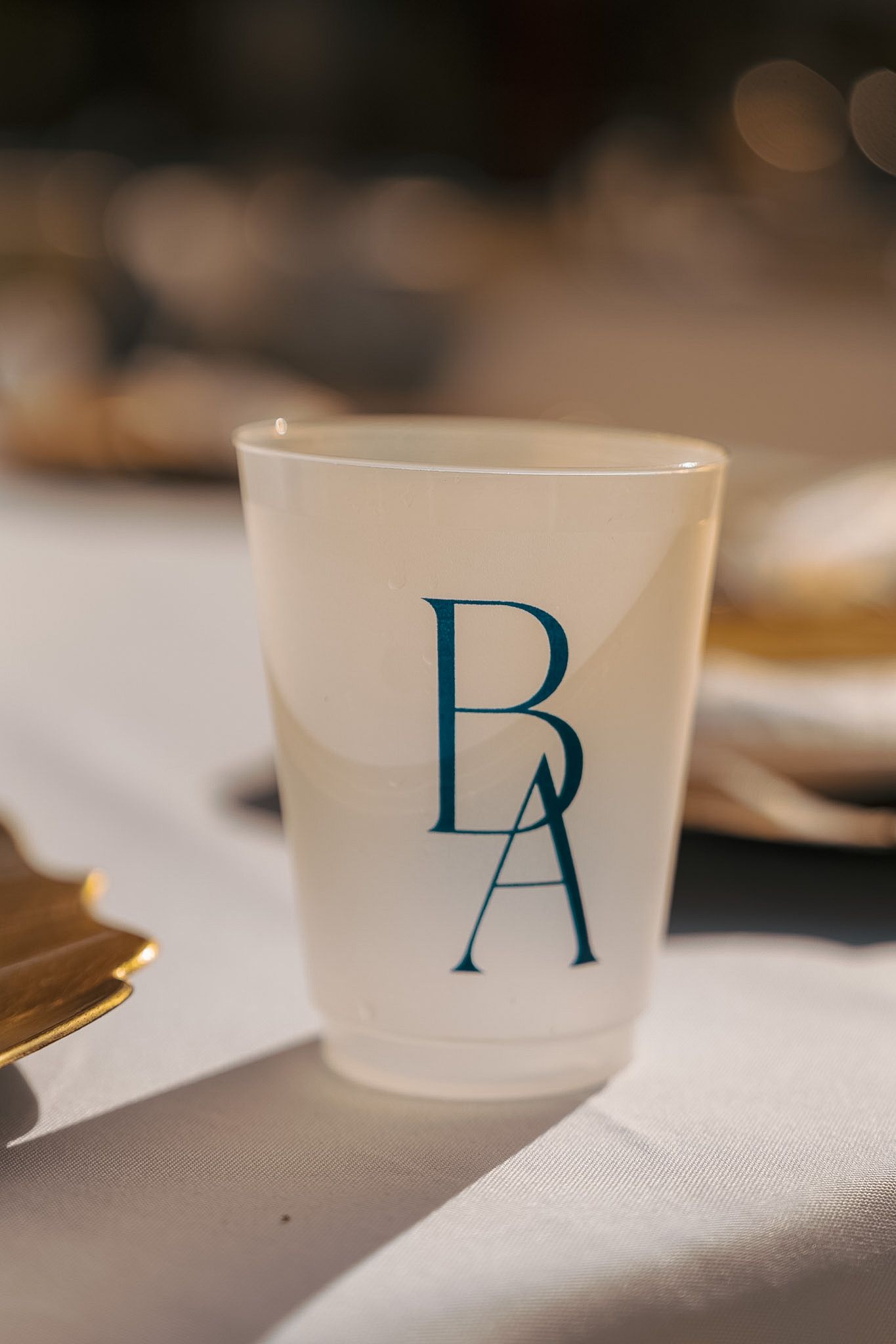 Custom frosted cup with monogram initials BA in teal on a white tablecloth at a wedding reception.