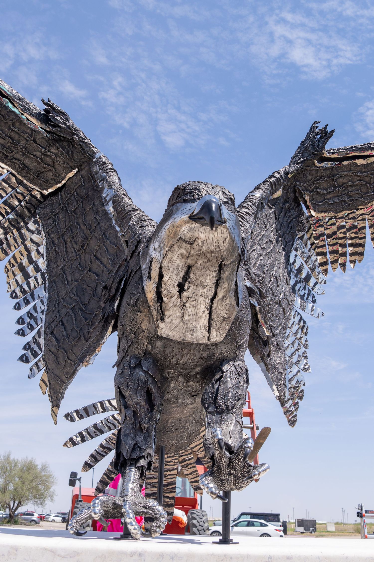 Large metal eagle sculpture with spread wings against a blue sky, showcasing intricate feather details in weathered steel.