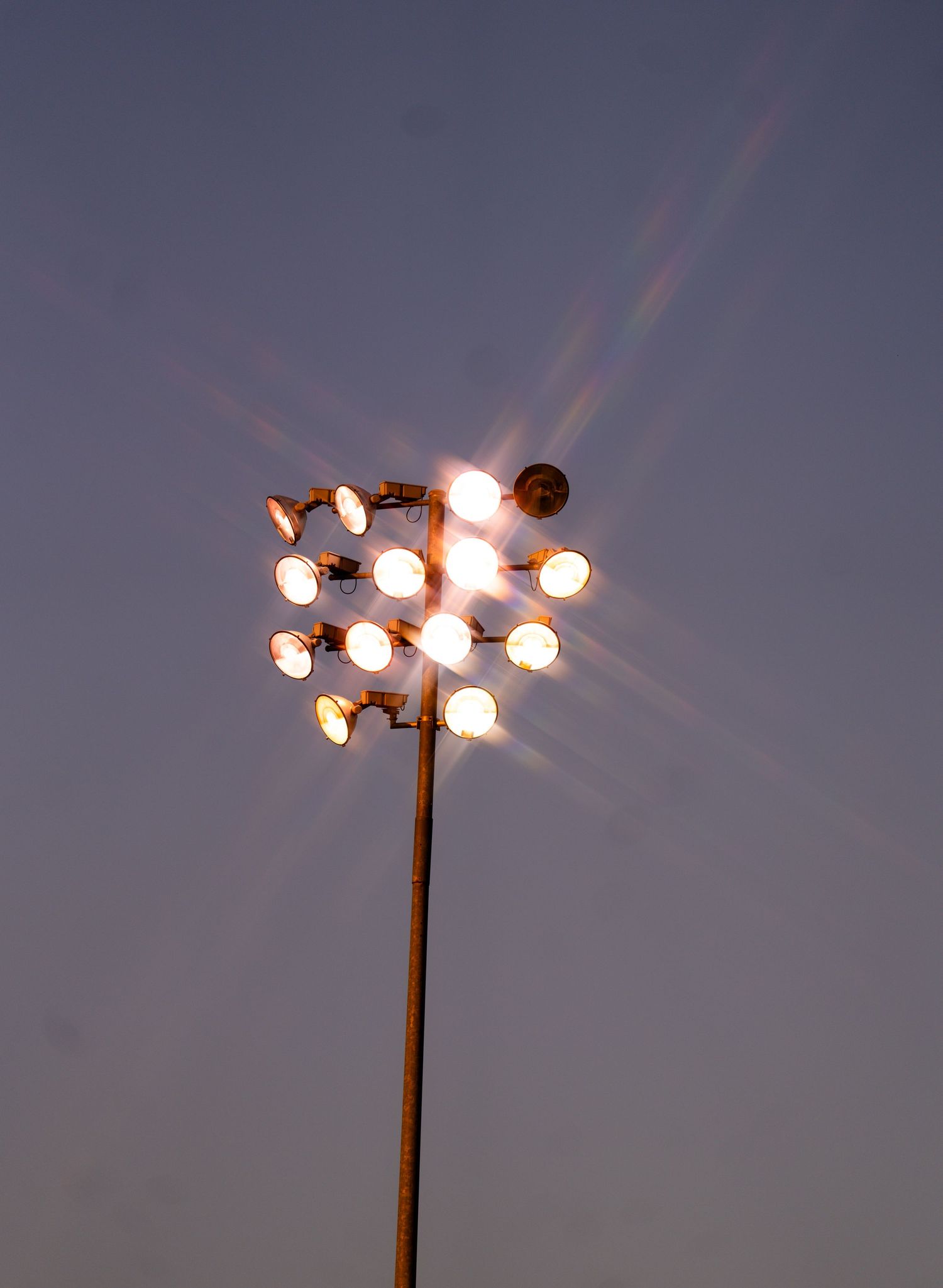 Bright stadium floodlights on a tall metal pole glowing against a dusk sky.