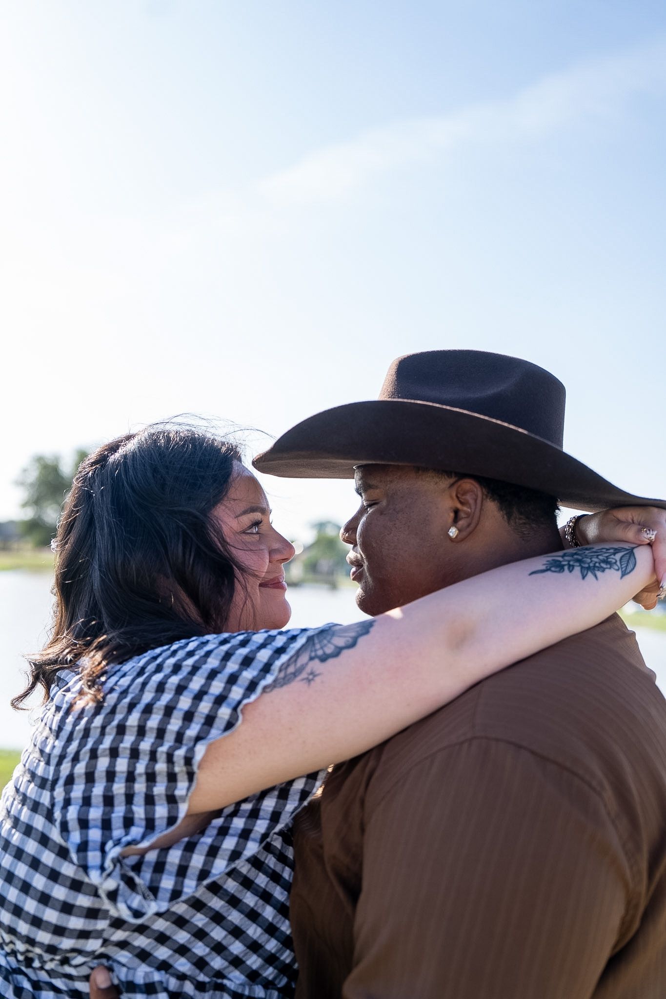 Happy interracial couple embracing and smiling at each other outdoors near water.