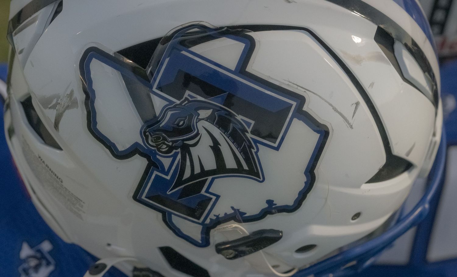 White football helmet featuring a blue Trinitas logo with a horse mascot and state outline design.