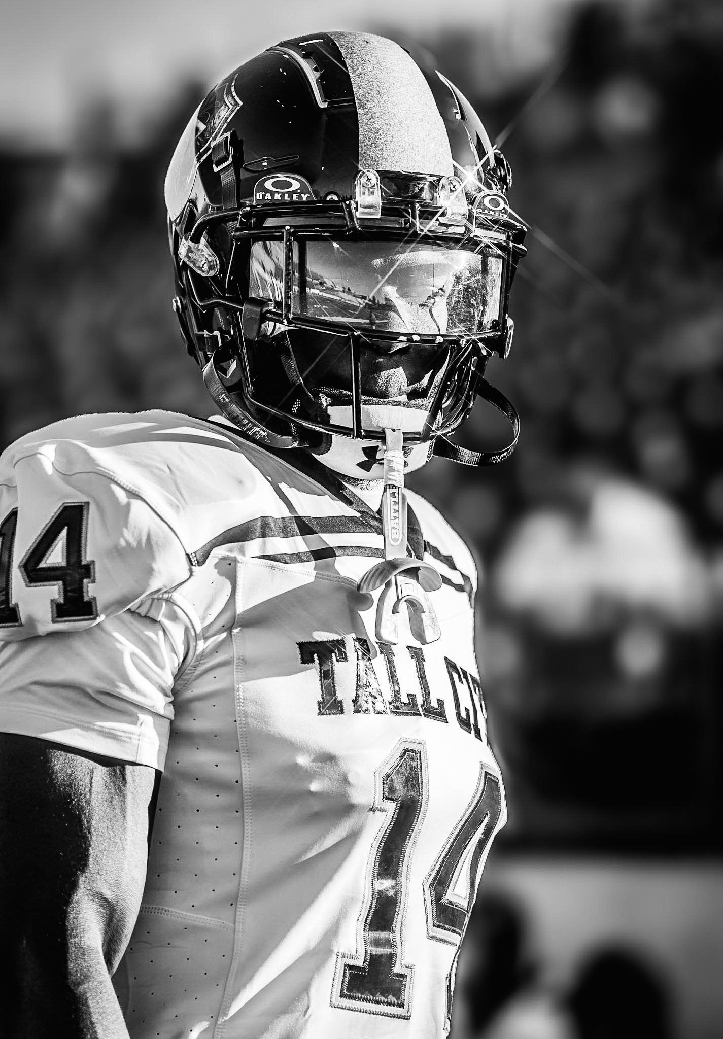 Black and white close-up of Tall City football player #14 wearing helmet with visor on sideline.