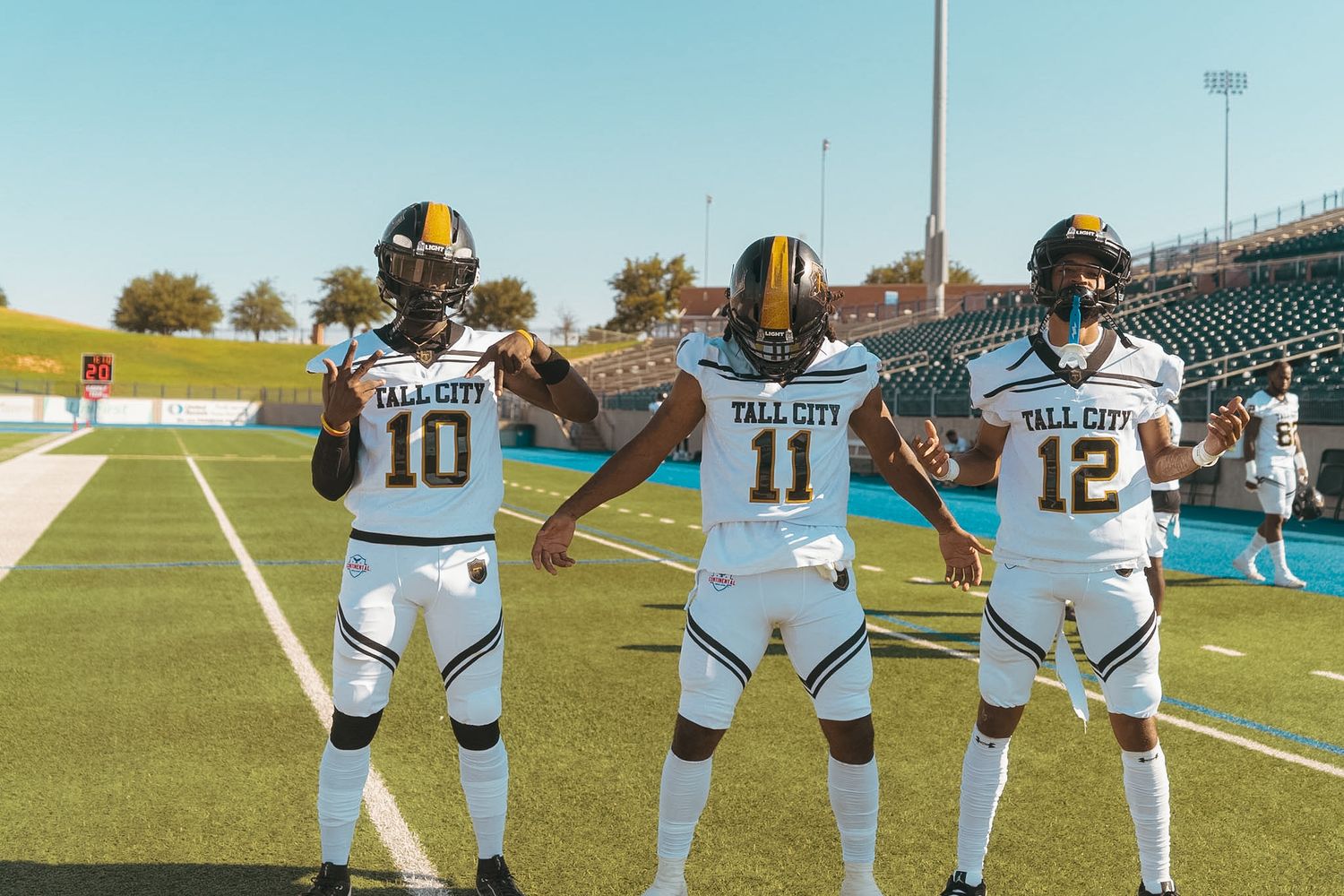 Three Tall City football players #10, #11, #12 posing together in white uniforms on field.