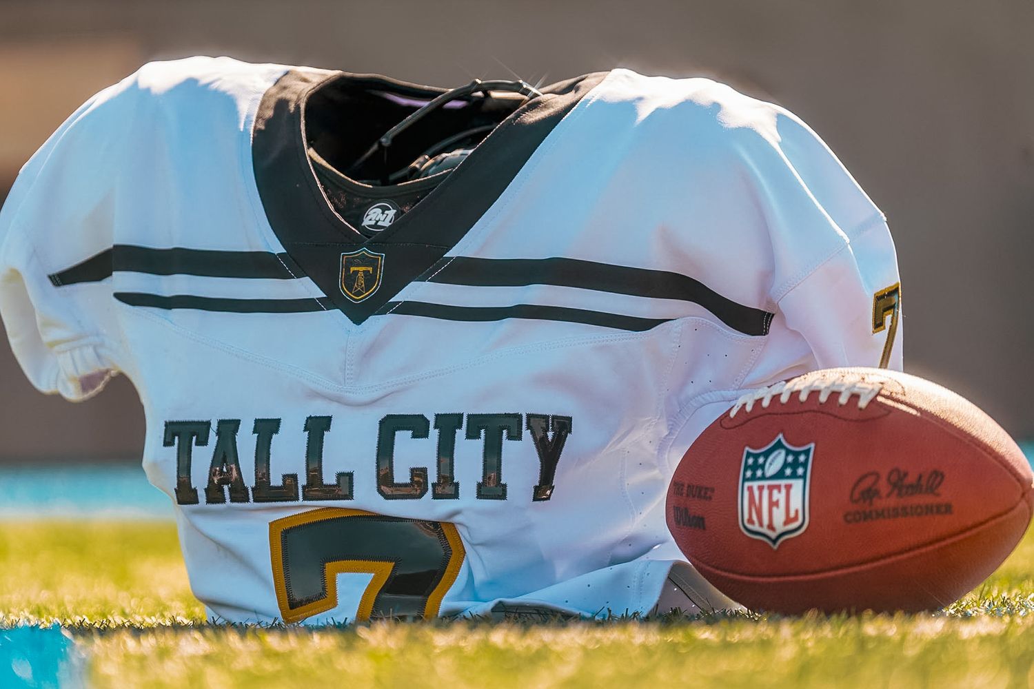 Tall City football jersey #7 and NFL football displayed on grass field in sunlight.