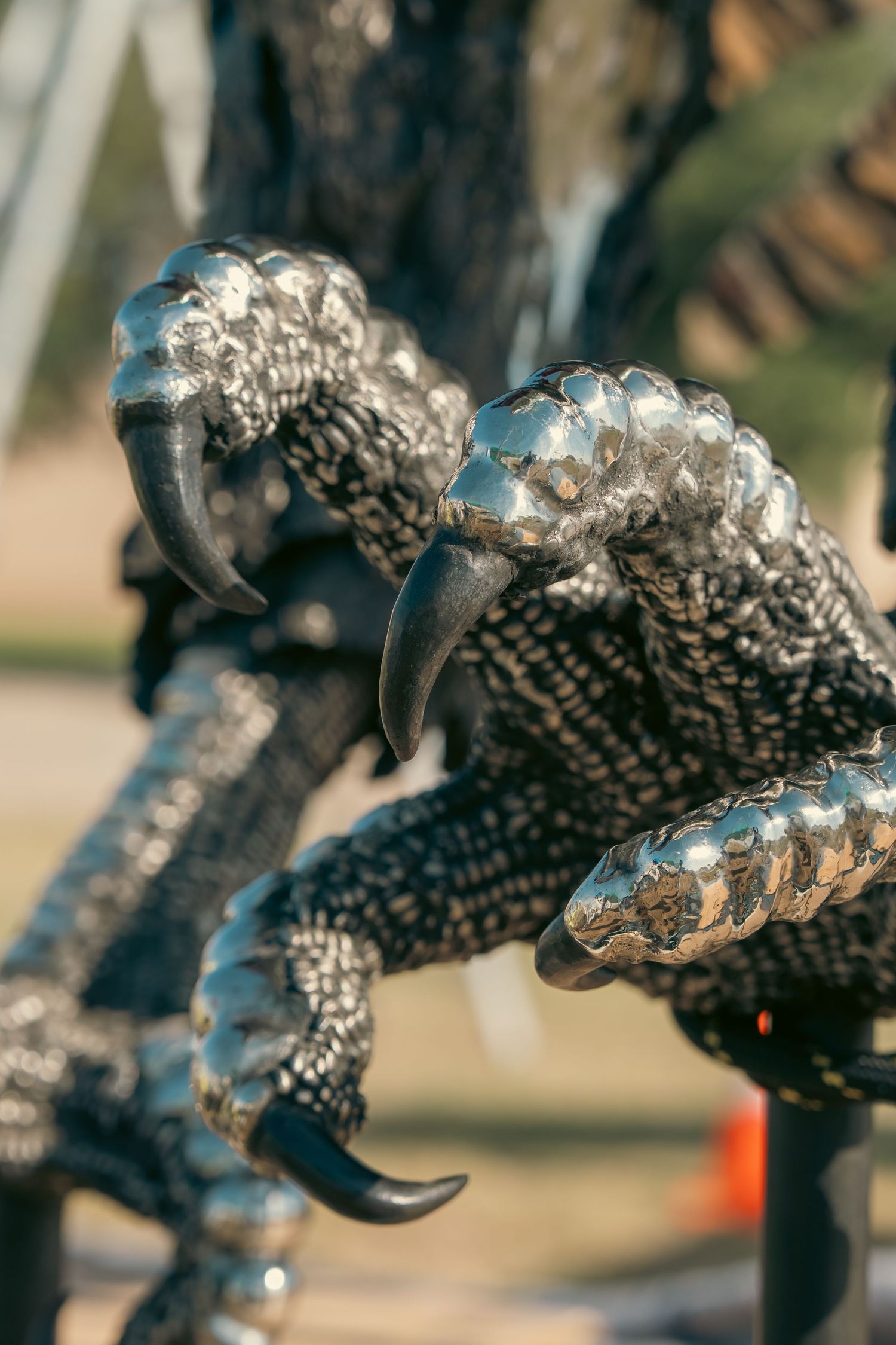Close-up of a metallic bird talon sculpture with shiny chrome scales and sharp black claws outdoors.