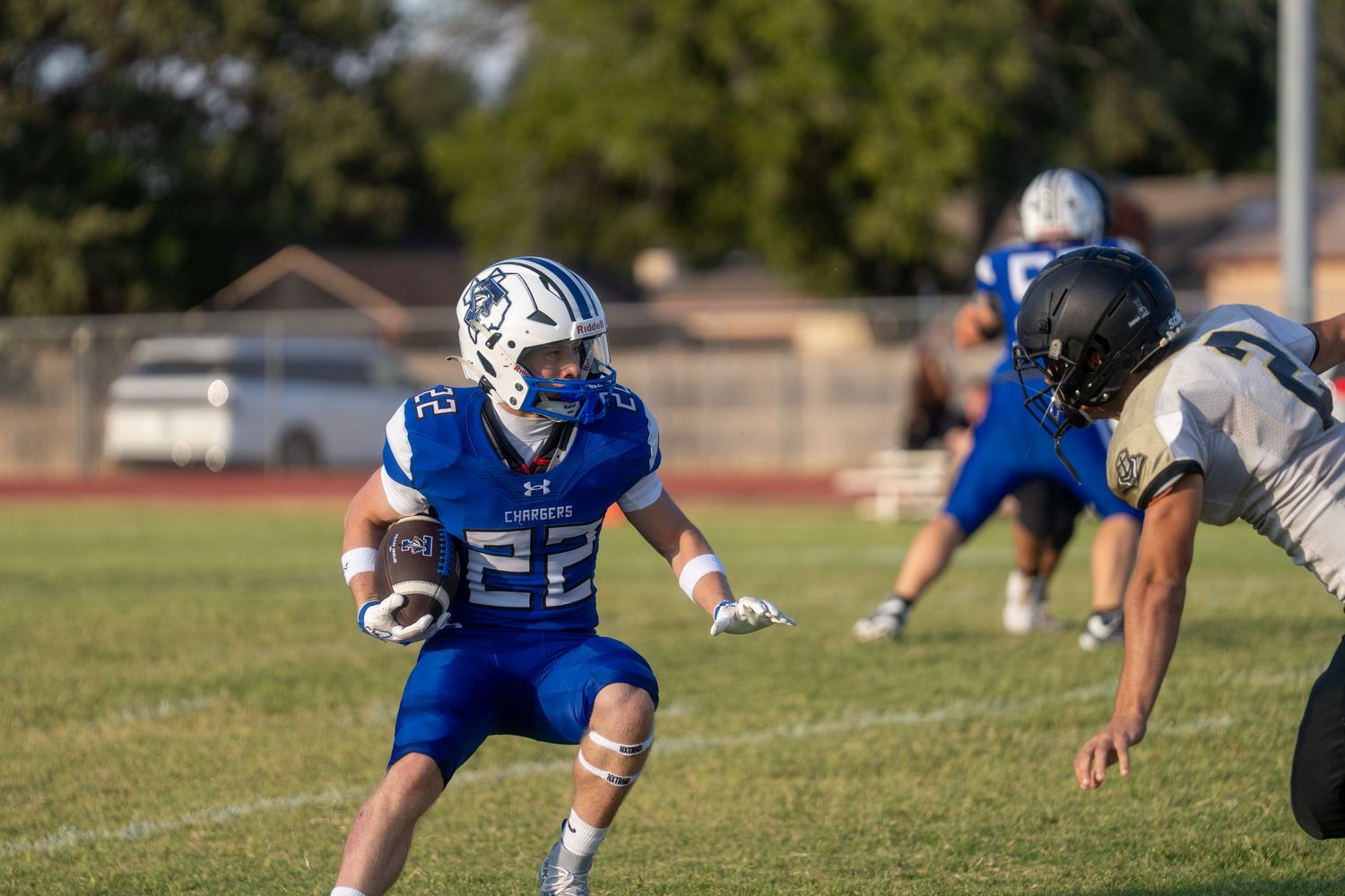 Football player #22 in blue uniform runs with the ball during a high school game under bright stadium lights.