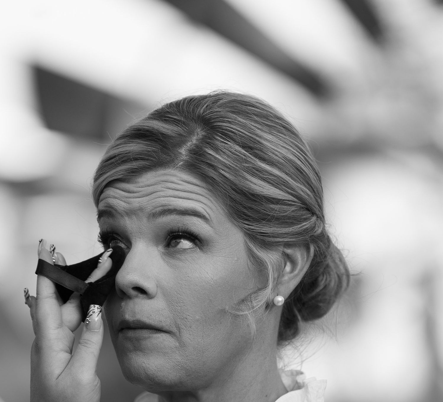 Bride in updo hairstyle dabs tears from her eye with tissue during emotional wedding ceremony moment.