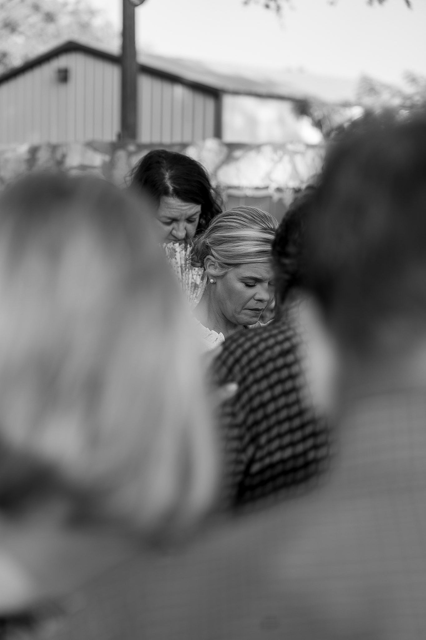 Black and white photo of bride with head bowed during wedding ceremony prayer.