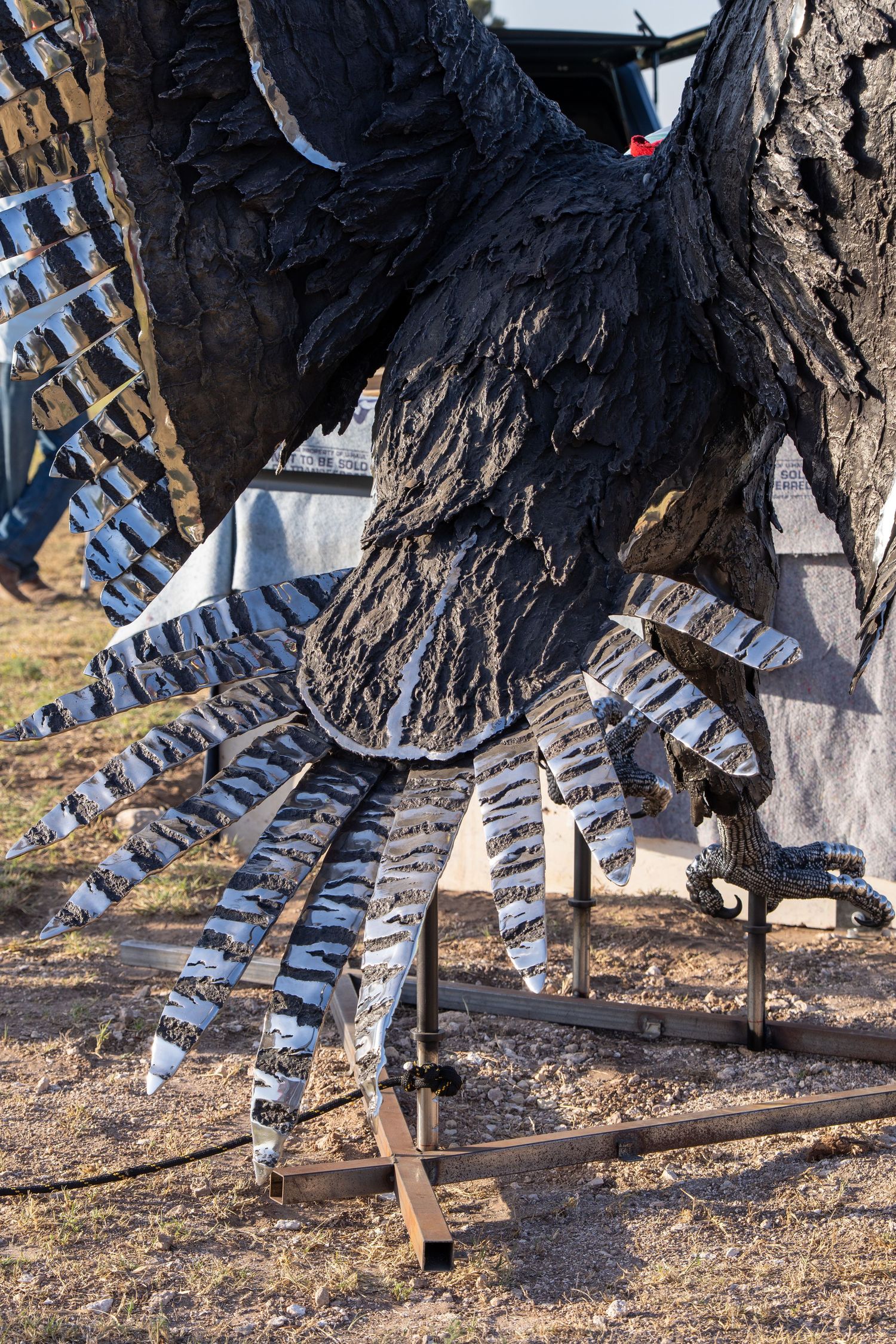 Large metal bird sculpture with detailed feathers and talons displayed outdoors near a tree.