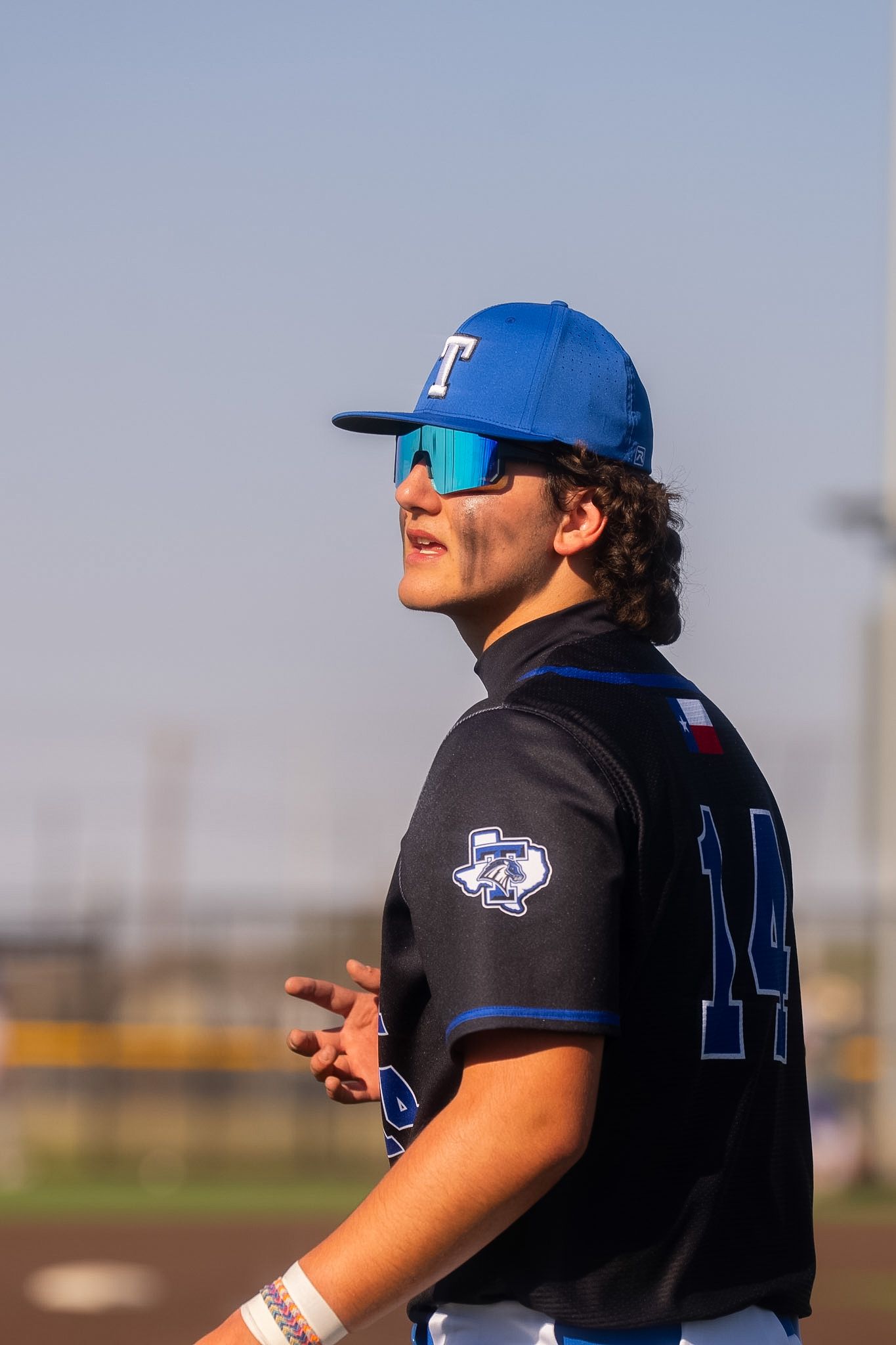 Baseball player #14 in blue Trinity cap and sunglasses on field.