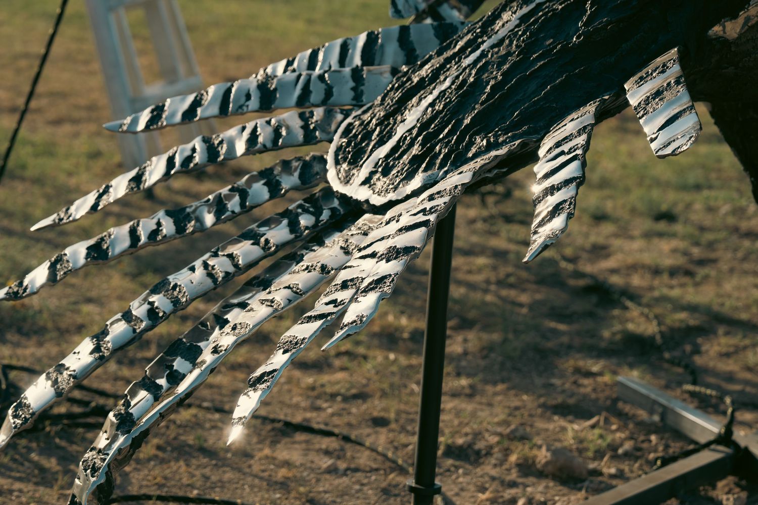 Close-up of a metal sculpture resembling a bird wing or claw, crafted from welded steel strips outdoors.