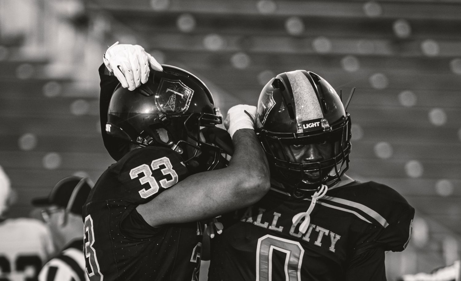 Two football players in black uniforms celebrate on the field, one wearing jersey number 33.