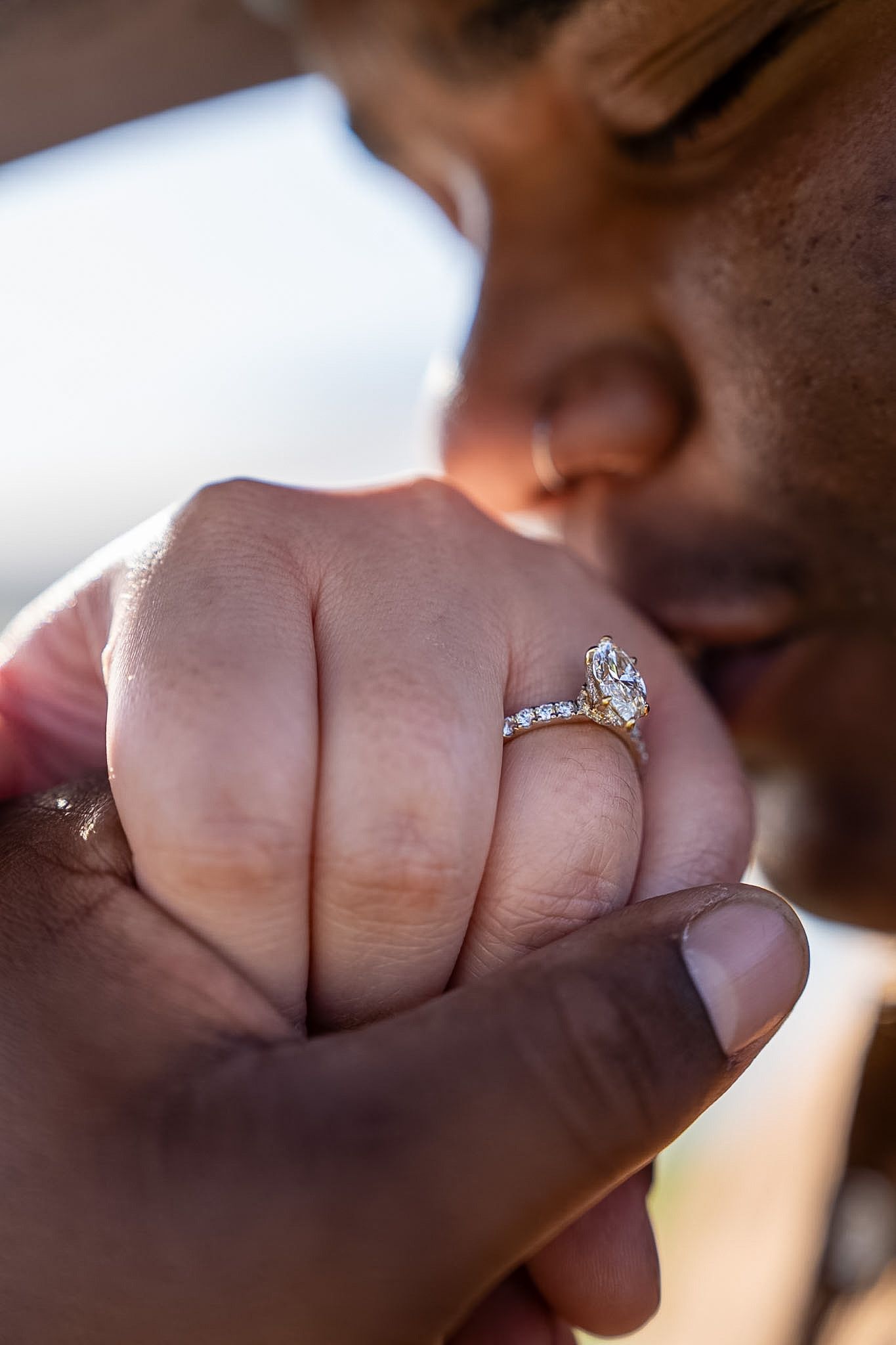 Man kissing womans hand adorned with a marquise diamond halo engagement ring.