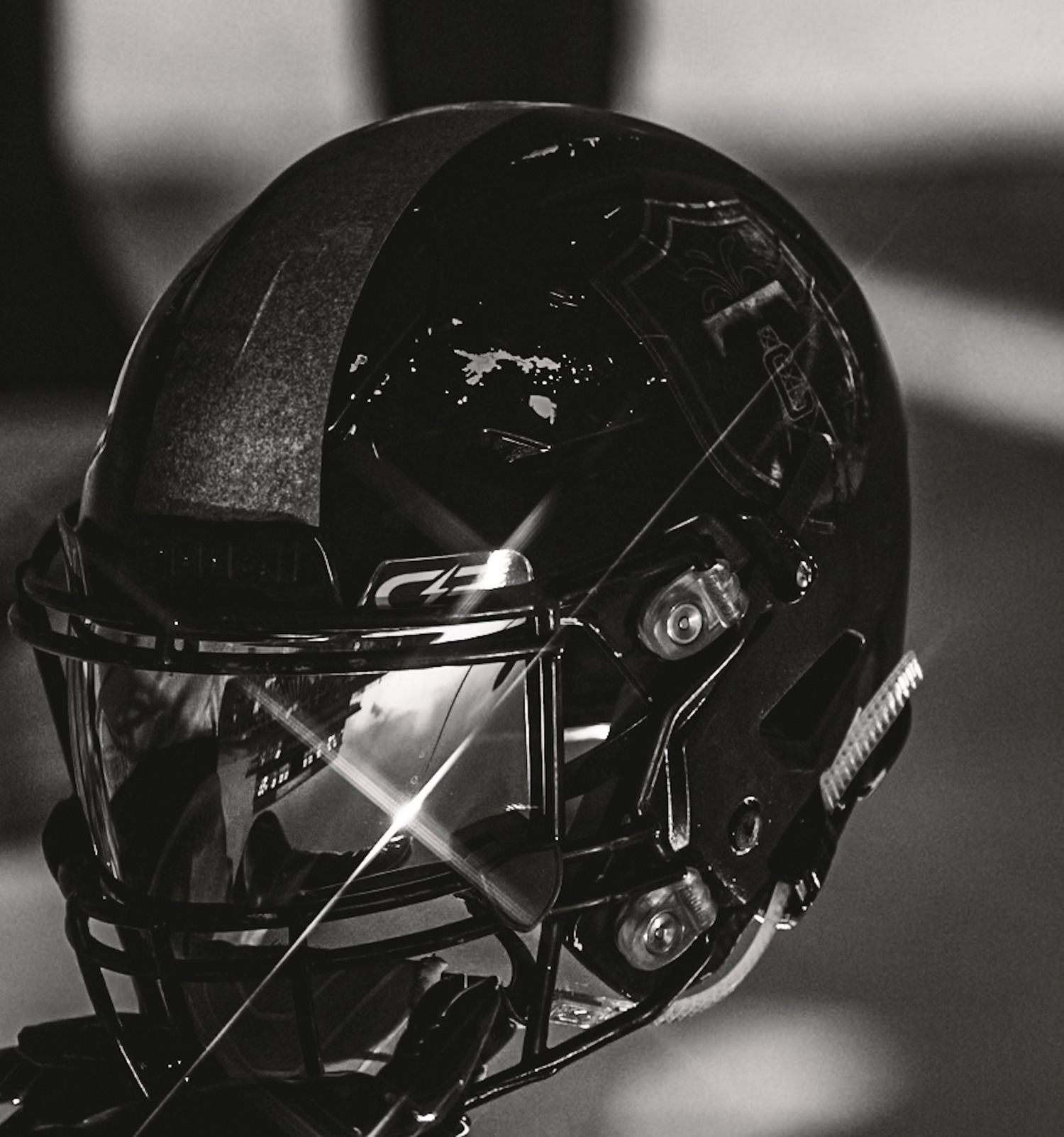 Sleek black football helmet with face mask in dramatic lighting.