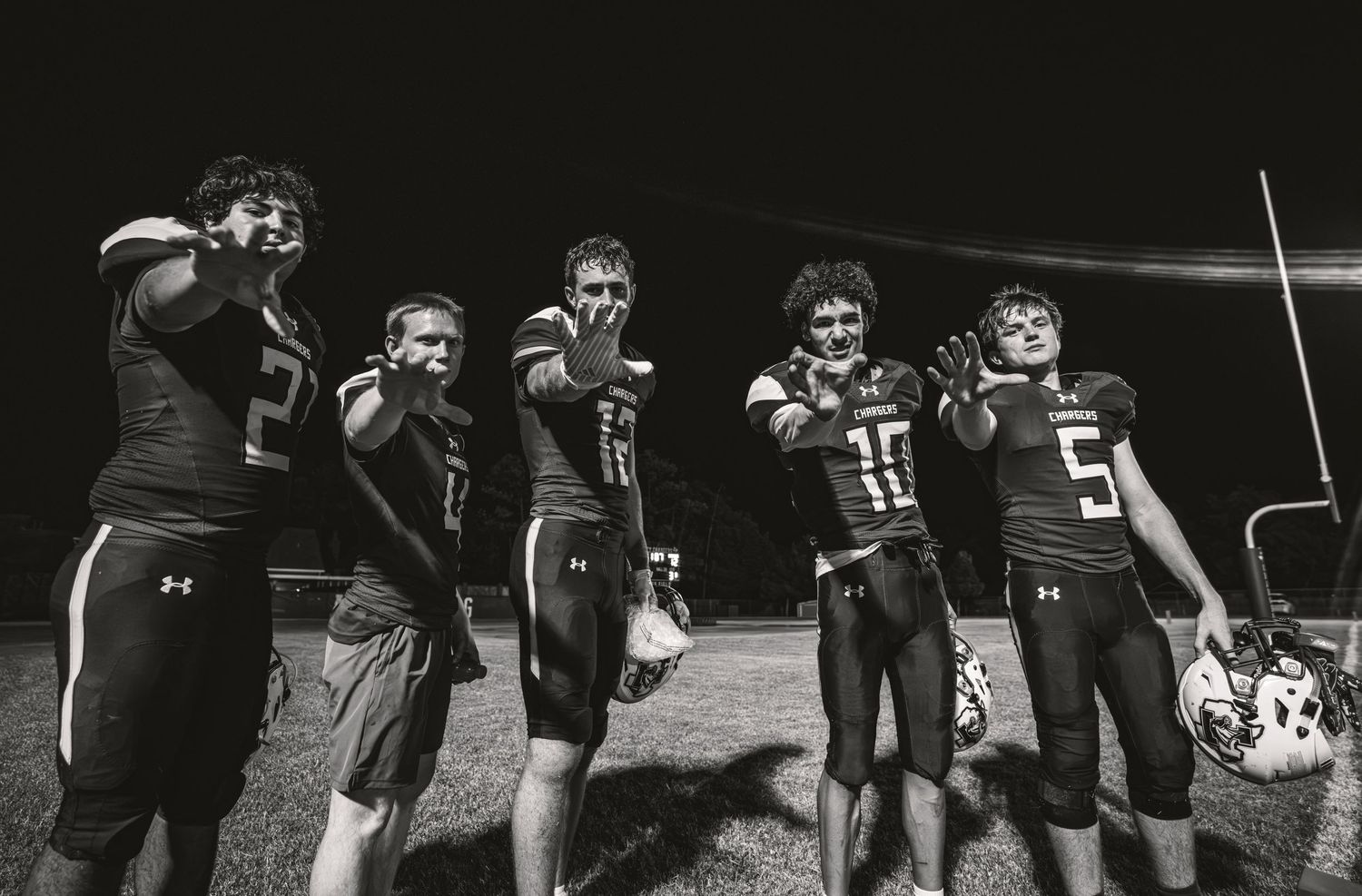 Five high school football players pose together on field at night in black and white photo wearing uniforms.