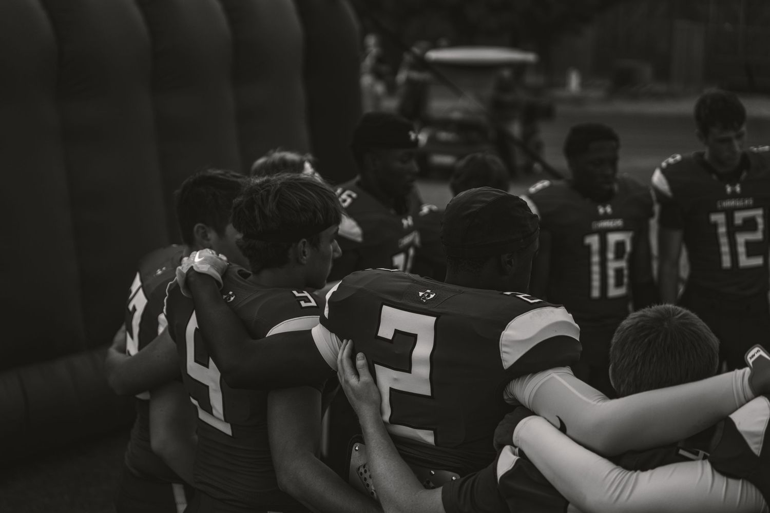 Black and white photo of youth football players huddling together on the sideline during a game.