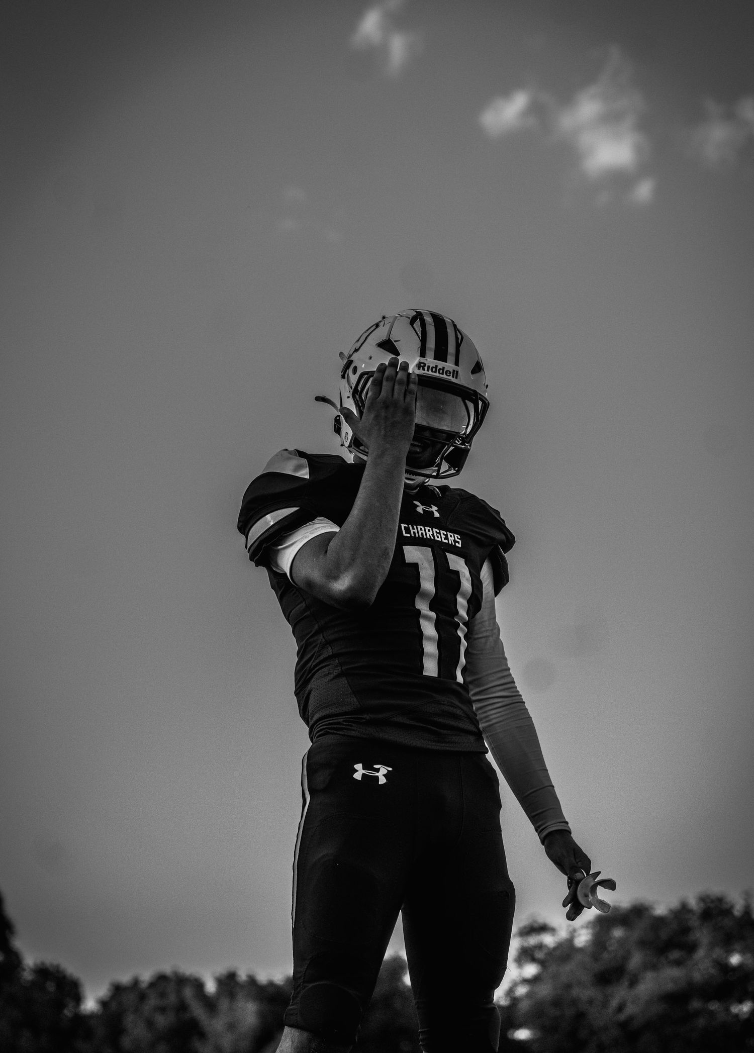 Black and white photo of football player #11 in Chargers uniform and helmet posing against cloudy sky.