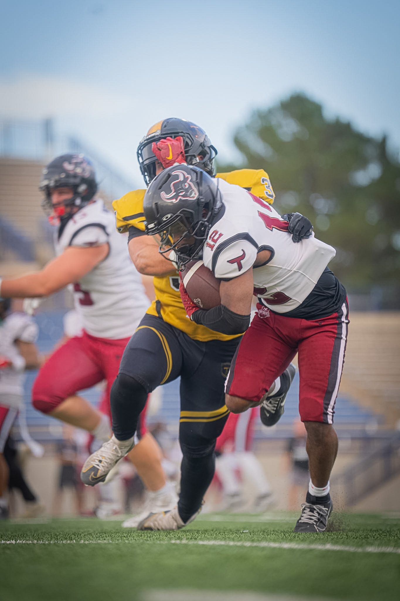 Football player in white jersey tackled by defender in black and gold uniform during game.