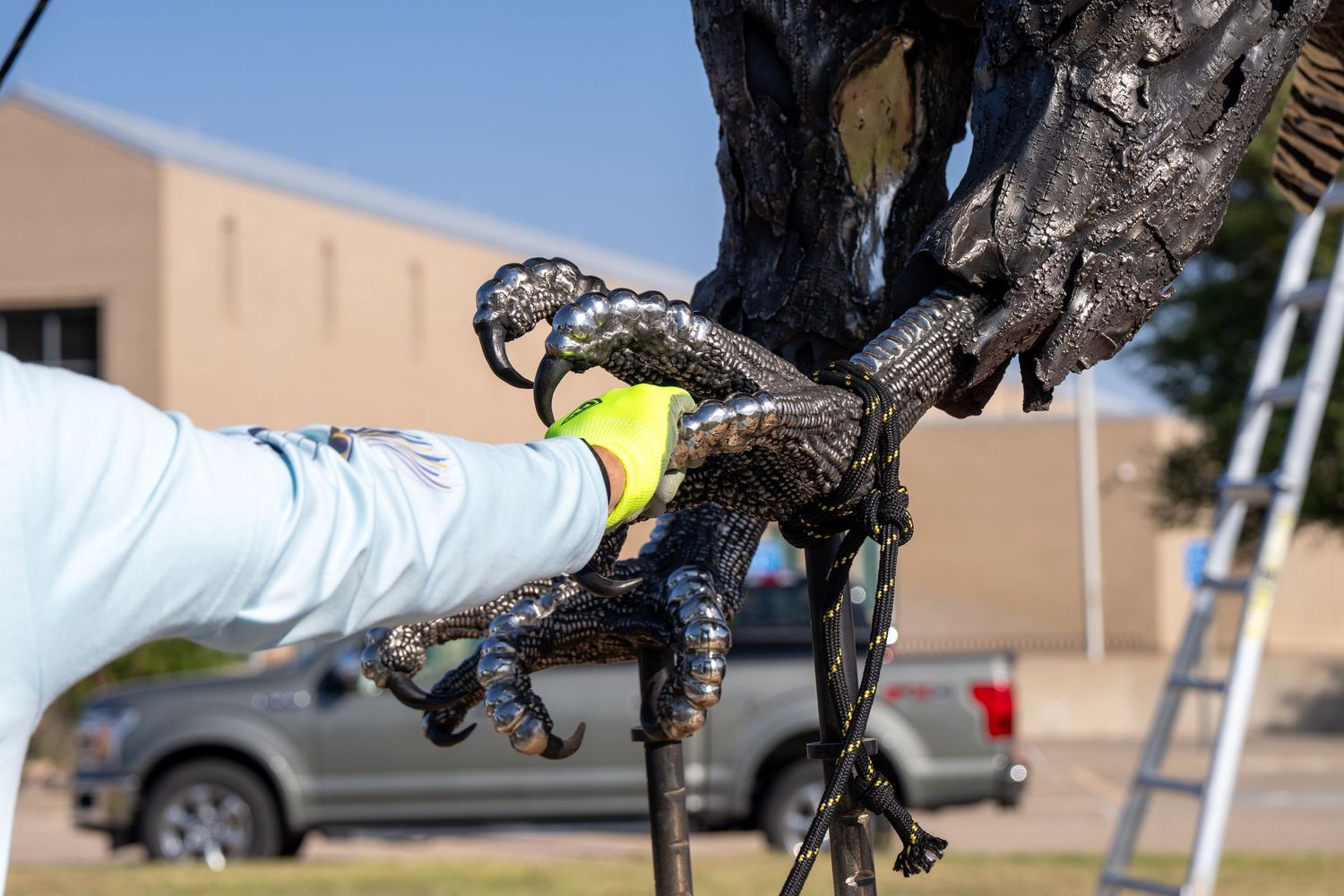 Worker in yellow gloves carefully handling a detailed dark metal bird sculpture outdoors.