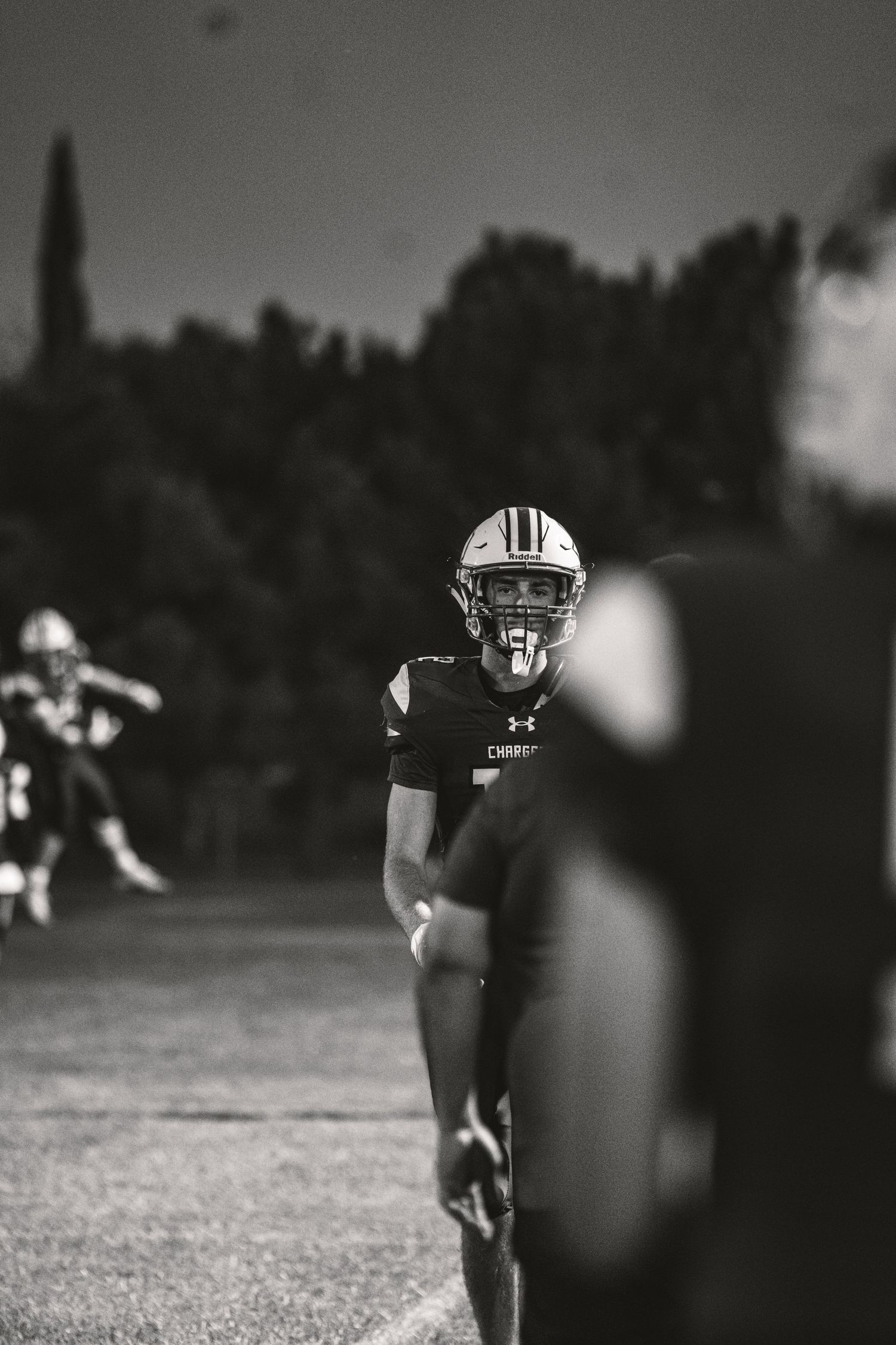 Black and white photo of a football player in helmet and uniform on field during a night game.
