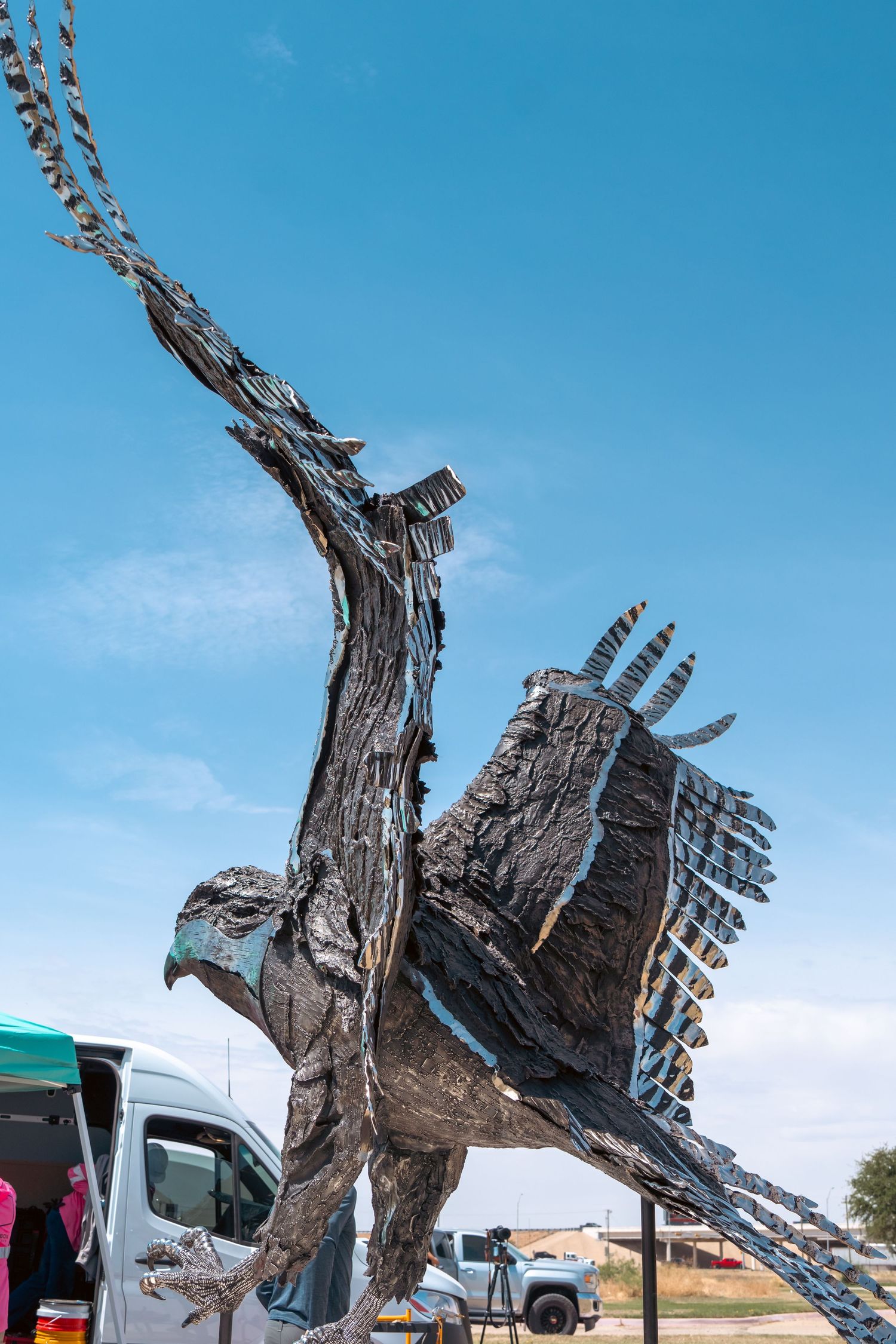 Large dramatic metal eagle sculpture with outstretched wings installed outdoors under blue sky.
