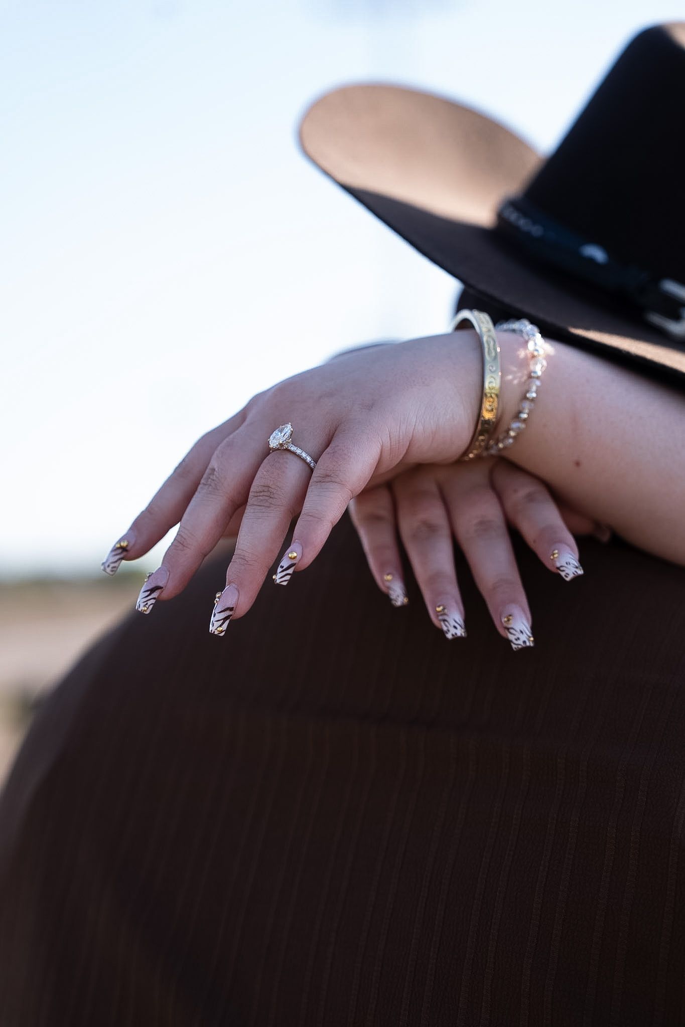 Close-up of womans hand with marquise engagement ring and gold bracelets on mans shoulder.