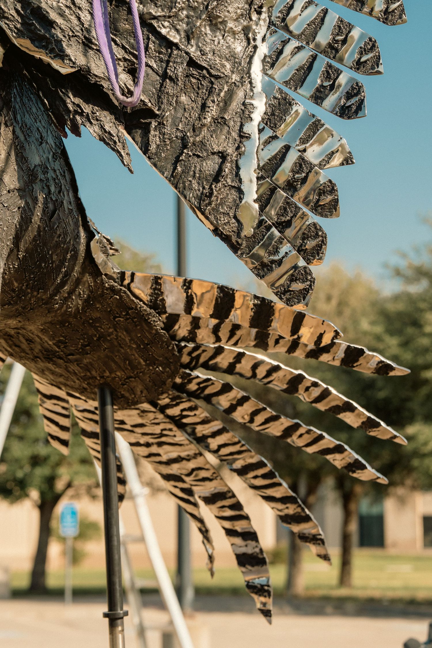 Close-up of large metal eagle sculpture talons with striped feather detail against blue sky.