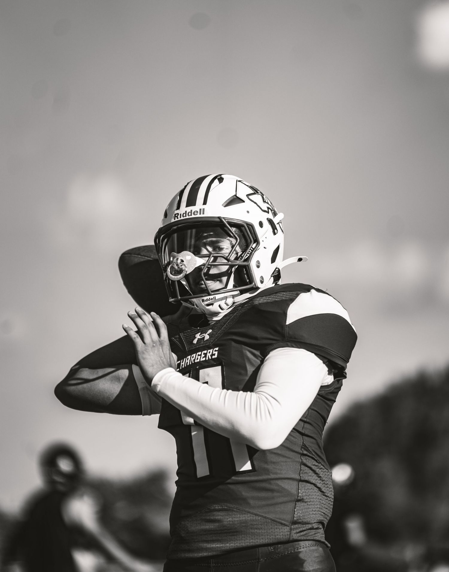 Black and white photo of a football quarterback in a Riddell helmet preparing to throw a pass during a game.