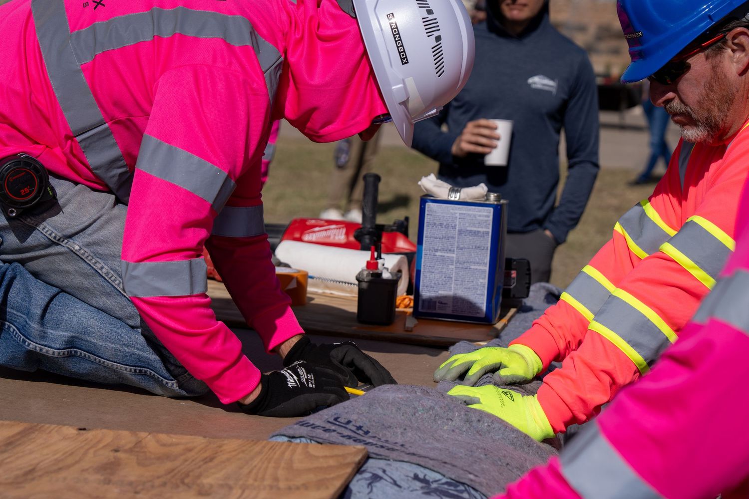 Workers in high-visibility safety gear and hard hats collaborate on a construction site task at an outdoor workstation.