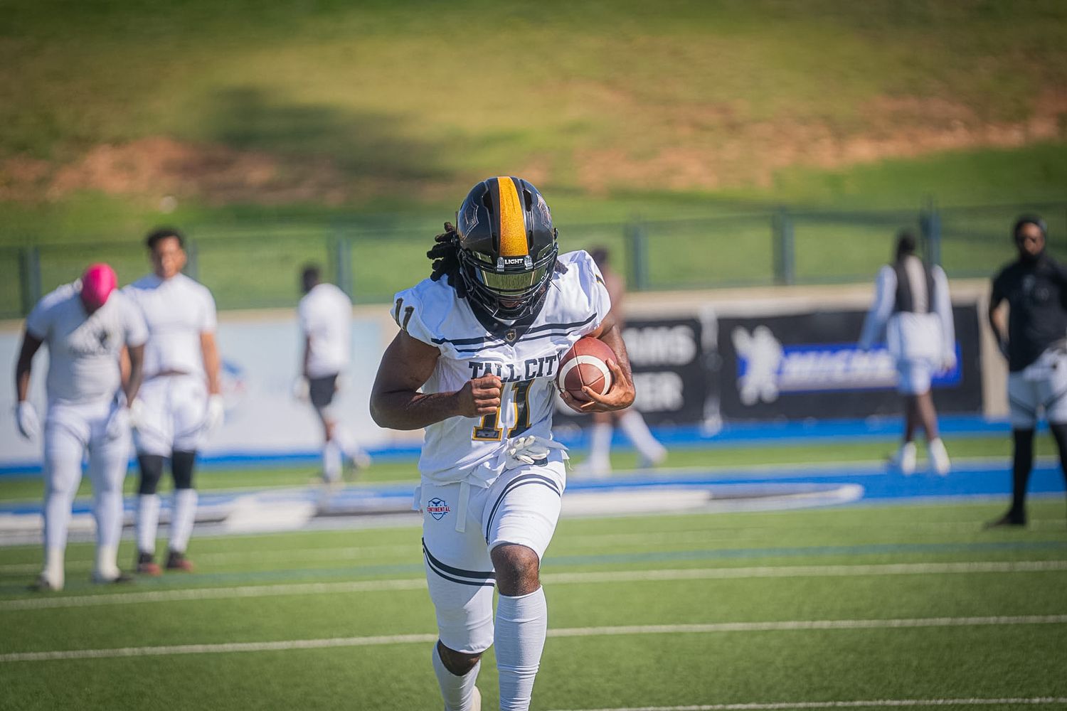 Tall City football player running with ball during game on blue turf field.
