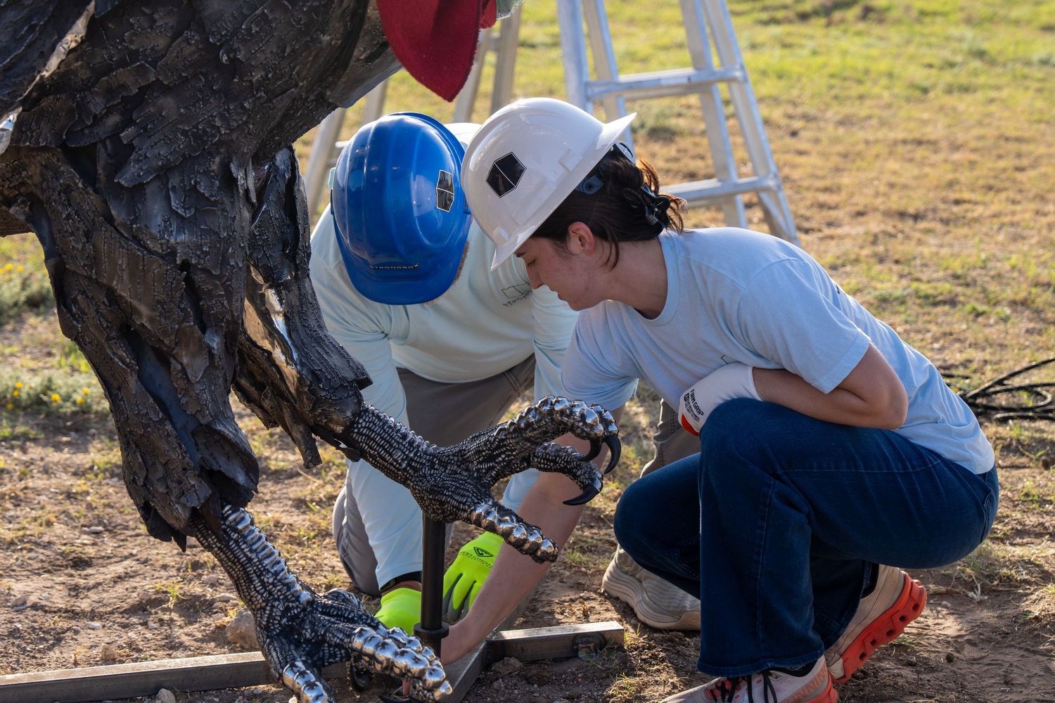 Two people in hard hats examining a large snake near a tree sculpture outdoors.