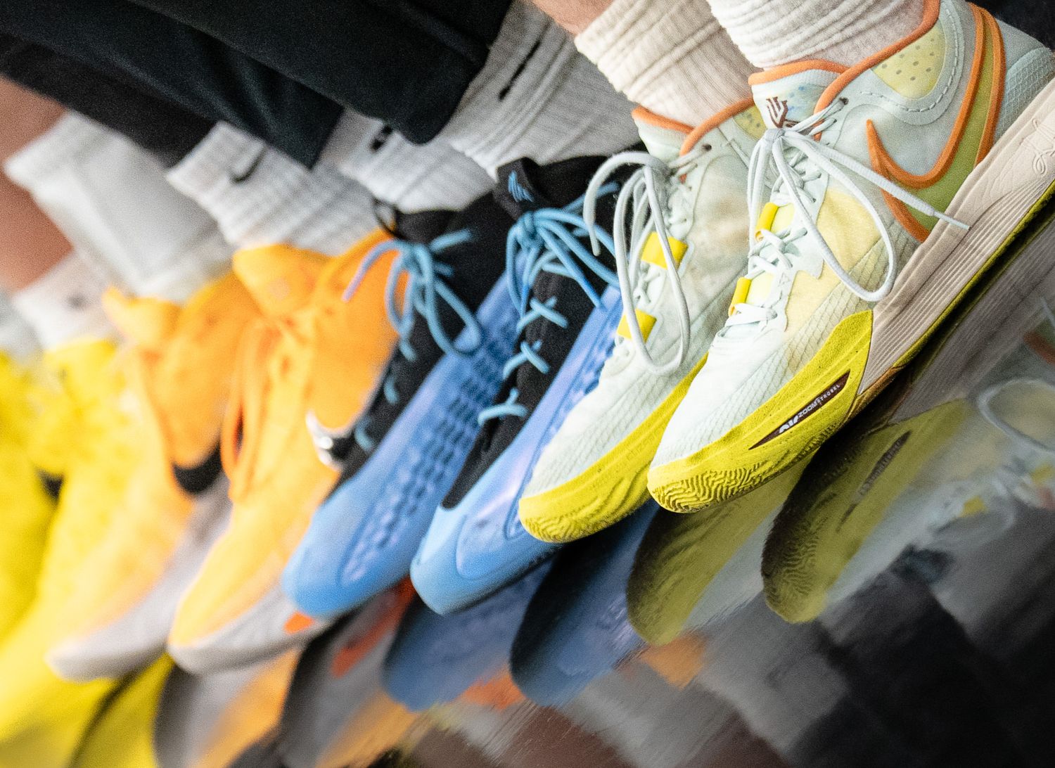 Colorful Nike basketball shoes lined up on a reflective surface in yellow, blue, and white.