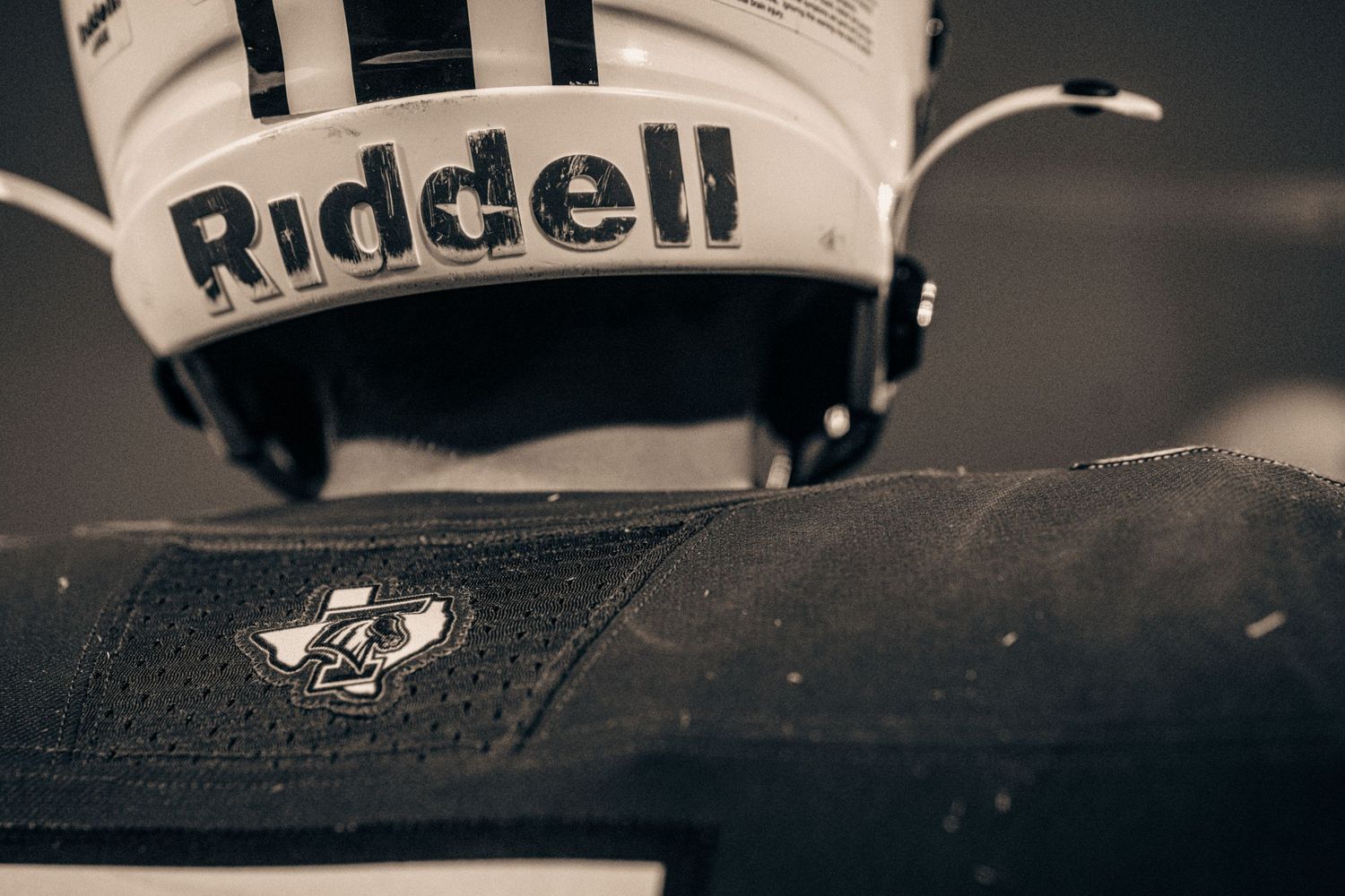 Close-up of a Riddell football helmet resting on a dark surface with a logo-embossed pad nearby.