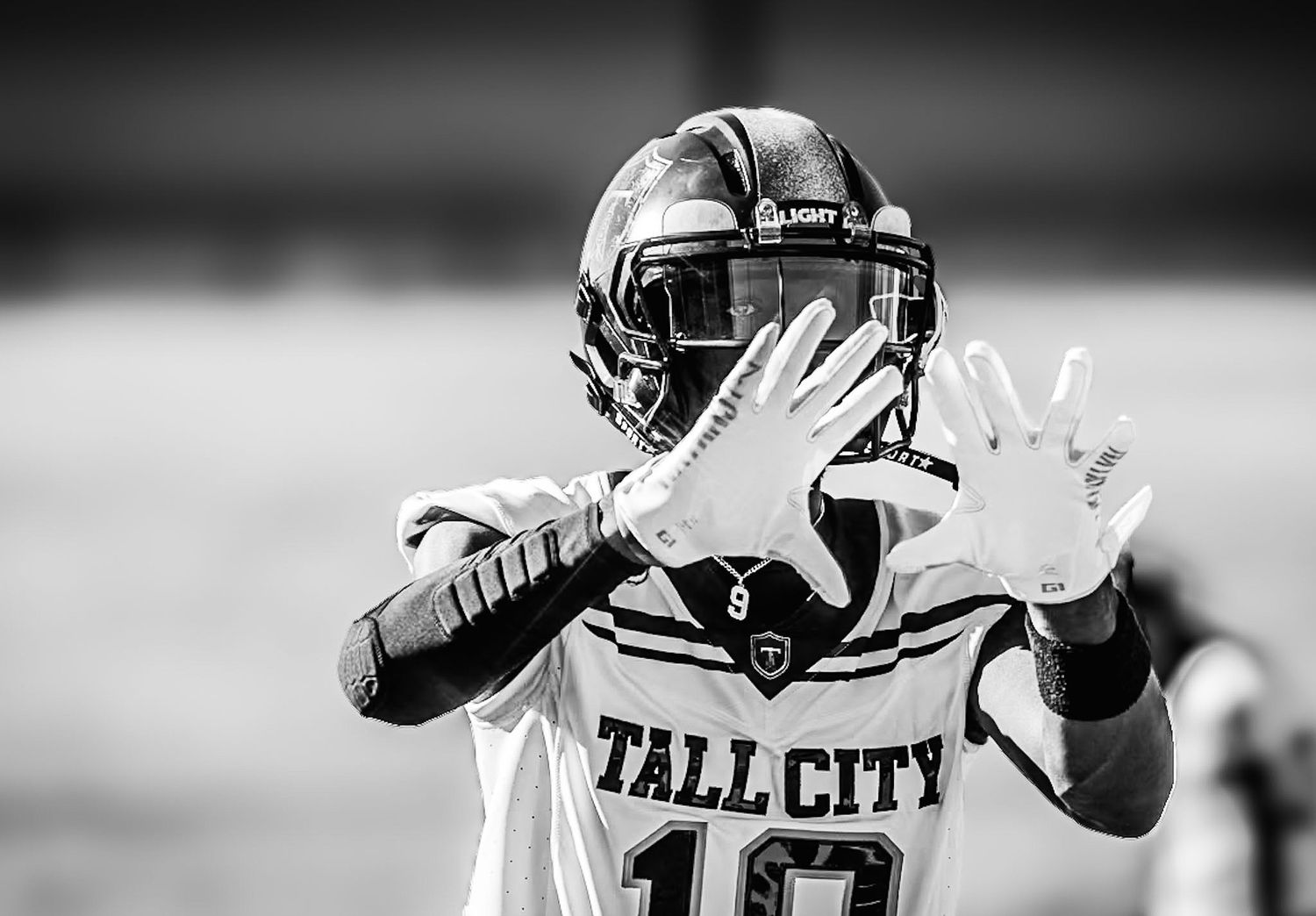 A football player in a white Tall City jersey number 10 raises his hands during a black and white game photo.
