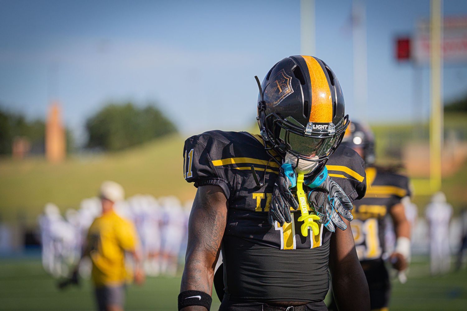 A Tall City football player in black and gold uniform stands on the sideline during a game.