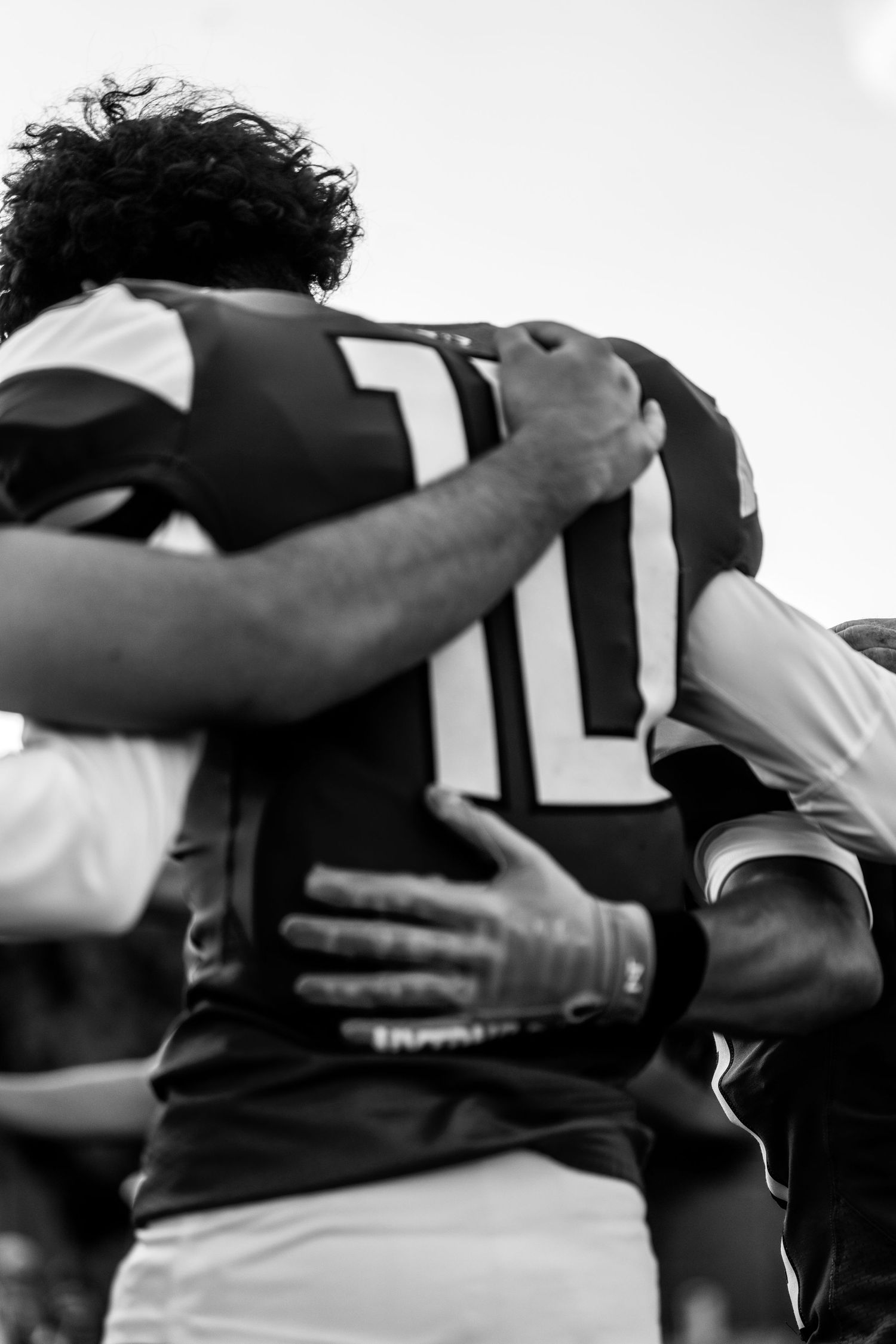 Black and white photo of rugby players in a team huddle, with player wearing number 10 jersey embraced by teammates.